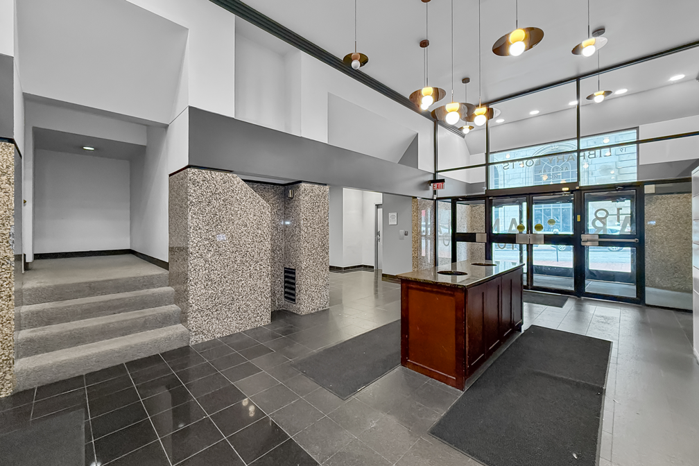 A spacious lobby featuring stone-tiled pillars, a small wooden front desk, a staircase, and glass double doors.