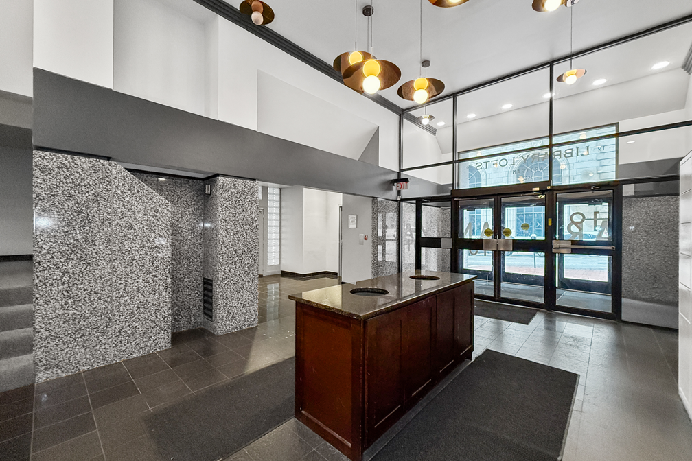 Modern lobby featuring a granite-tiled desk, black-framed glass entrance, and contemporary pendant lighting.