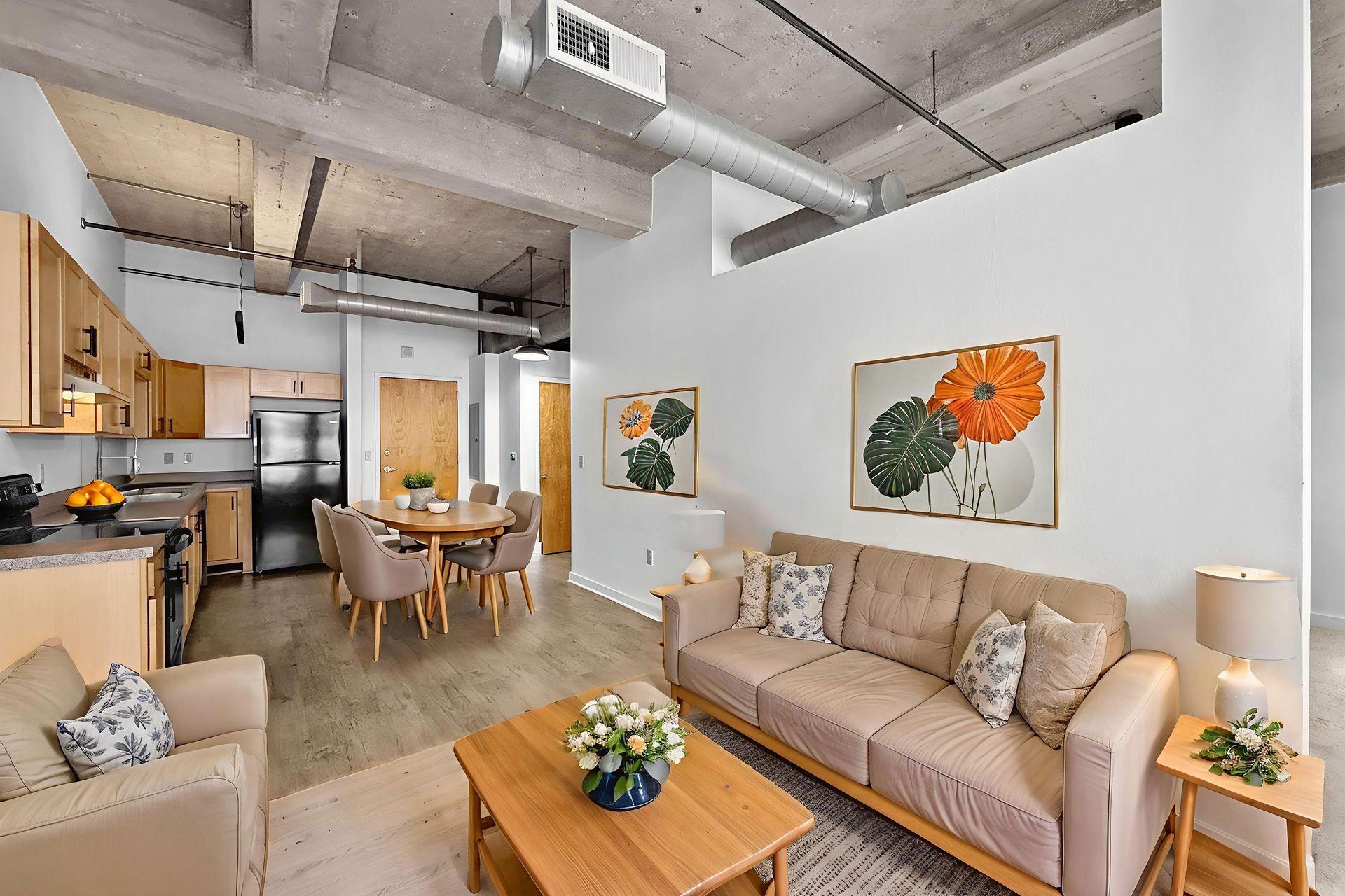 Modern open-concept loft with a kitchen, dining area, and living room featuring neutral furniture and exposed ceilings.