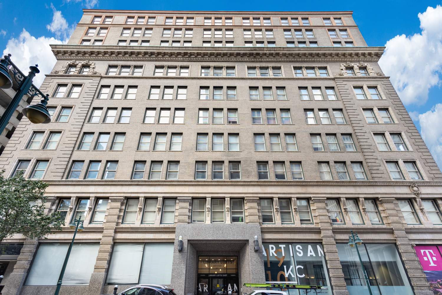 A multistory, stone-faced commercial building with a central entrance, ground-level retail, and a blue sky background.