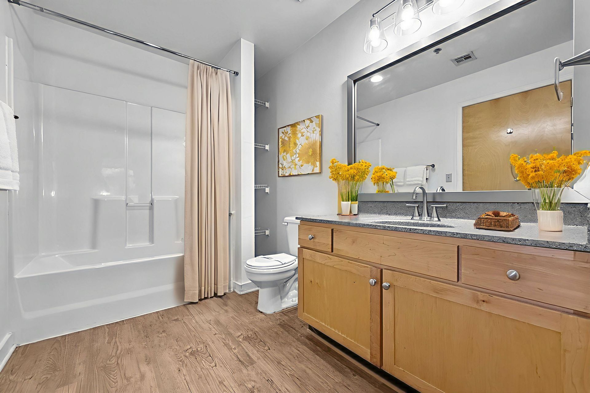 A bathroom with light wood cabinets, a granite vanity top, a white bathtub, and yellow floral accents on a light background.