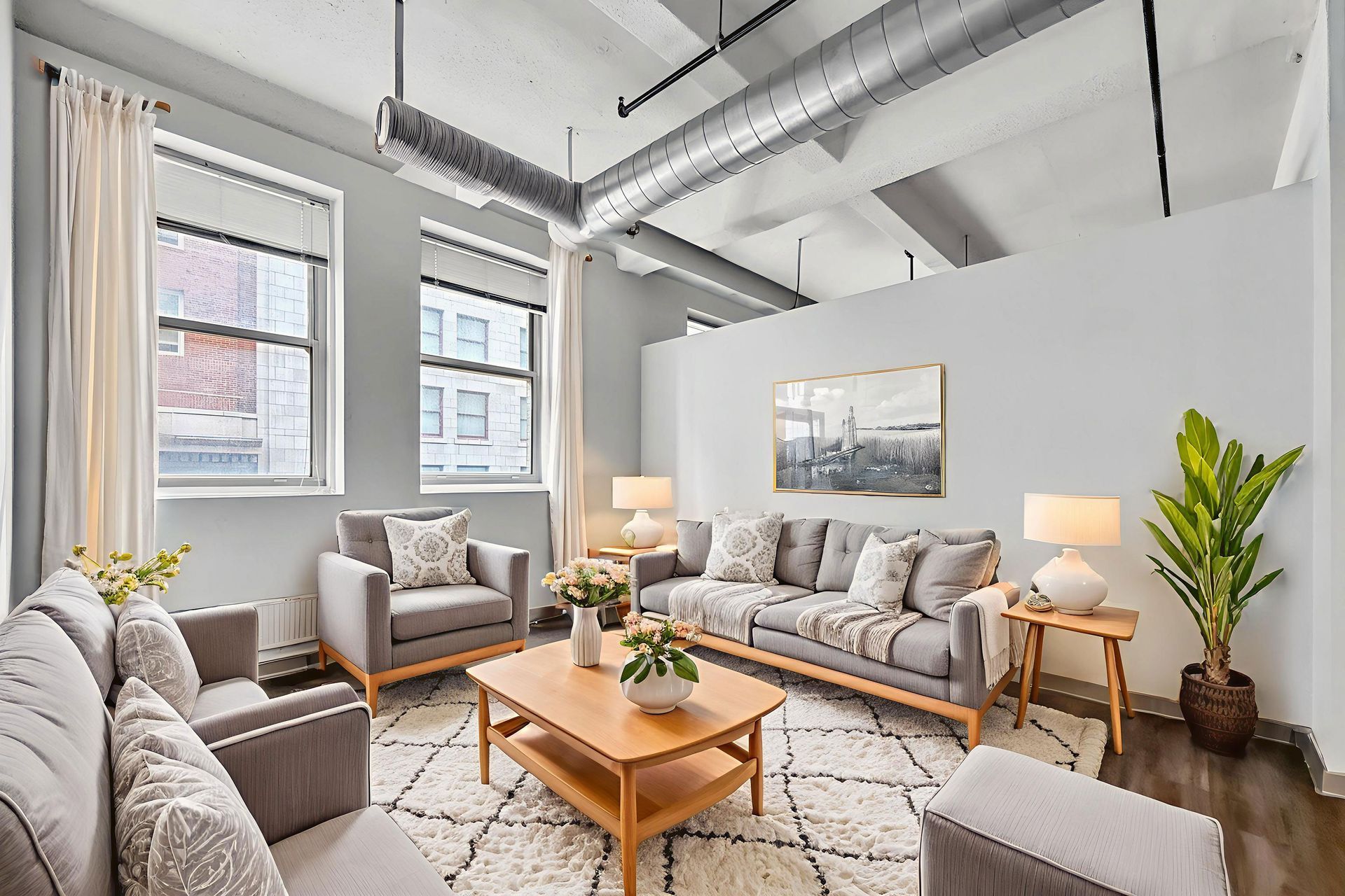 A bright living room with gray sofas, a wood coffee table, patterned rug, floor lamp, and a large potted plant.