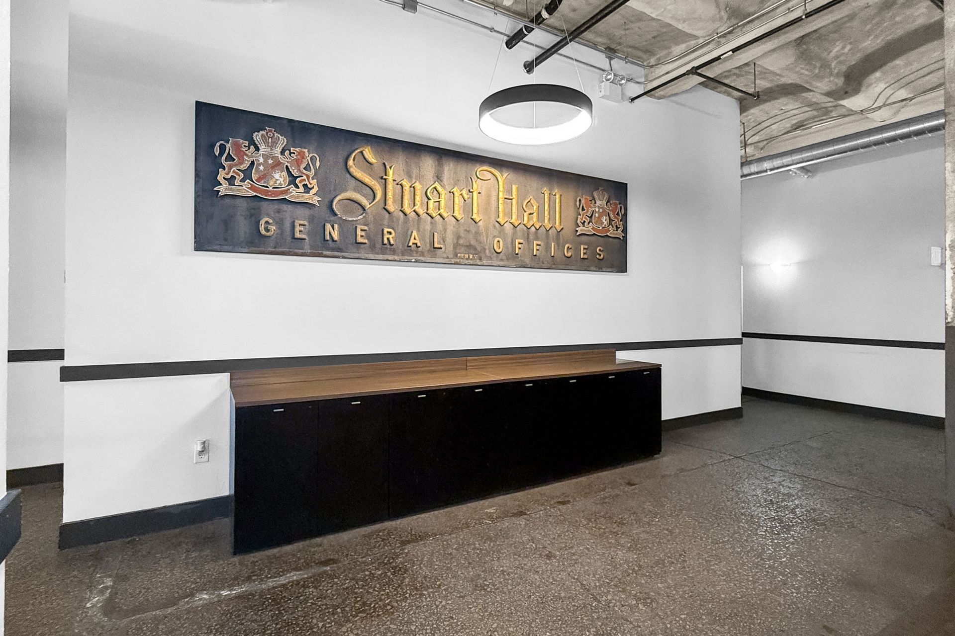 The Stuart Hall General M.D. office sign hangs above a dark reception desk in a modern, white-walled room with exposed ceiling.