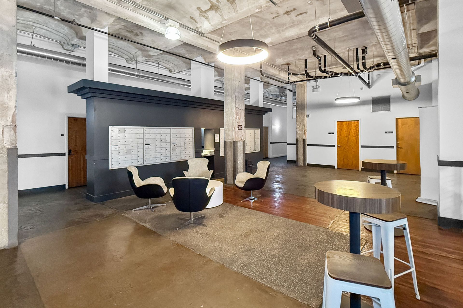 An industrial-style office lobby with concrete ceilings, a seating area with armchairs, and a high table with stools.