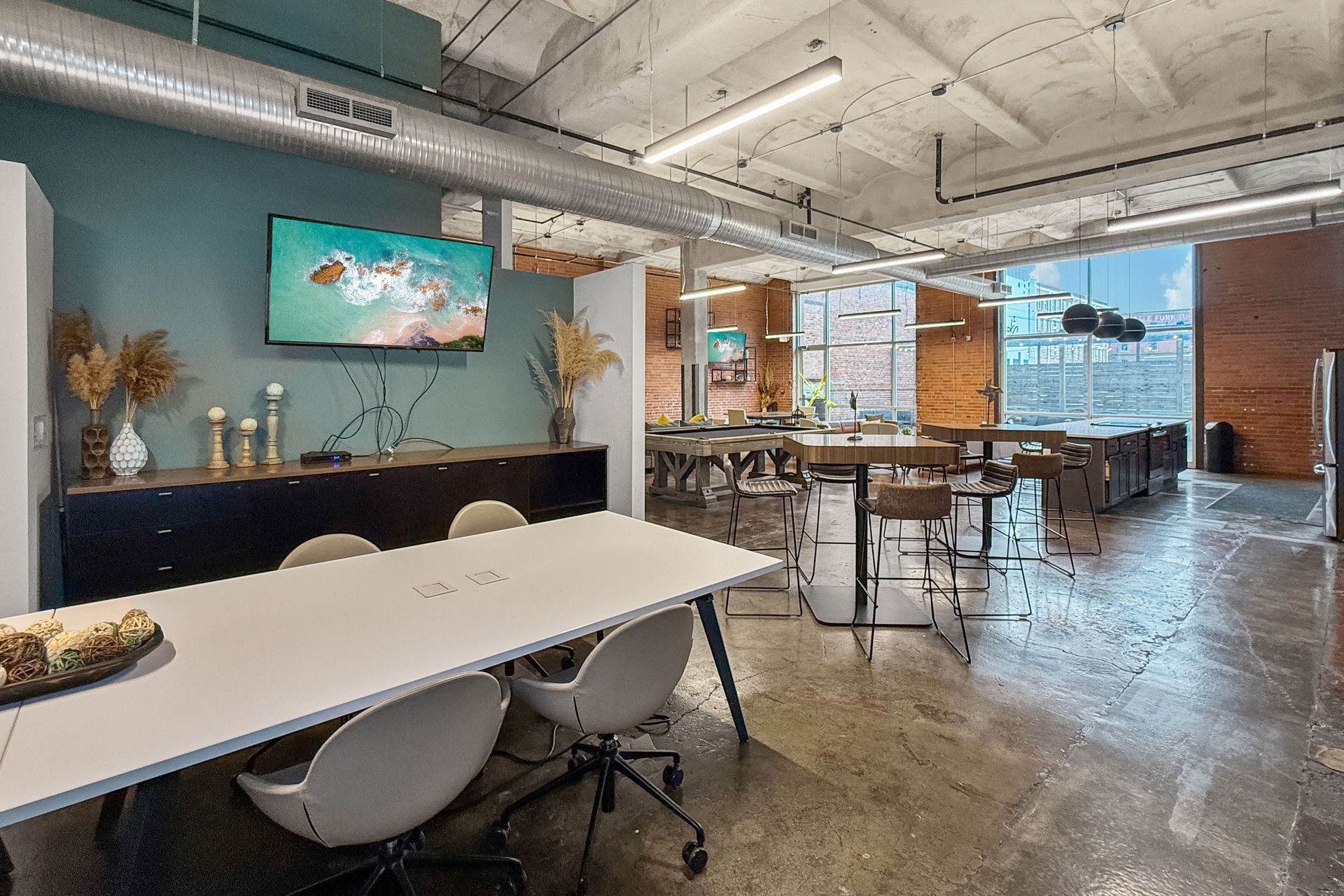 Modern office space featuring a white conference table, teal accent wall, flat-screen TV, and industrial concrete floors.