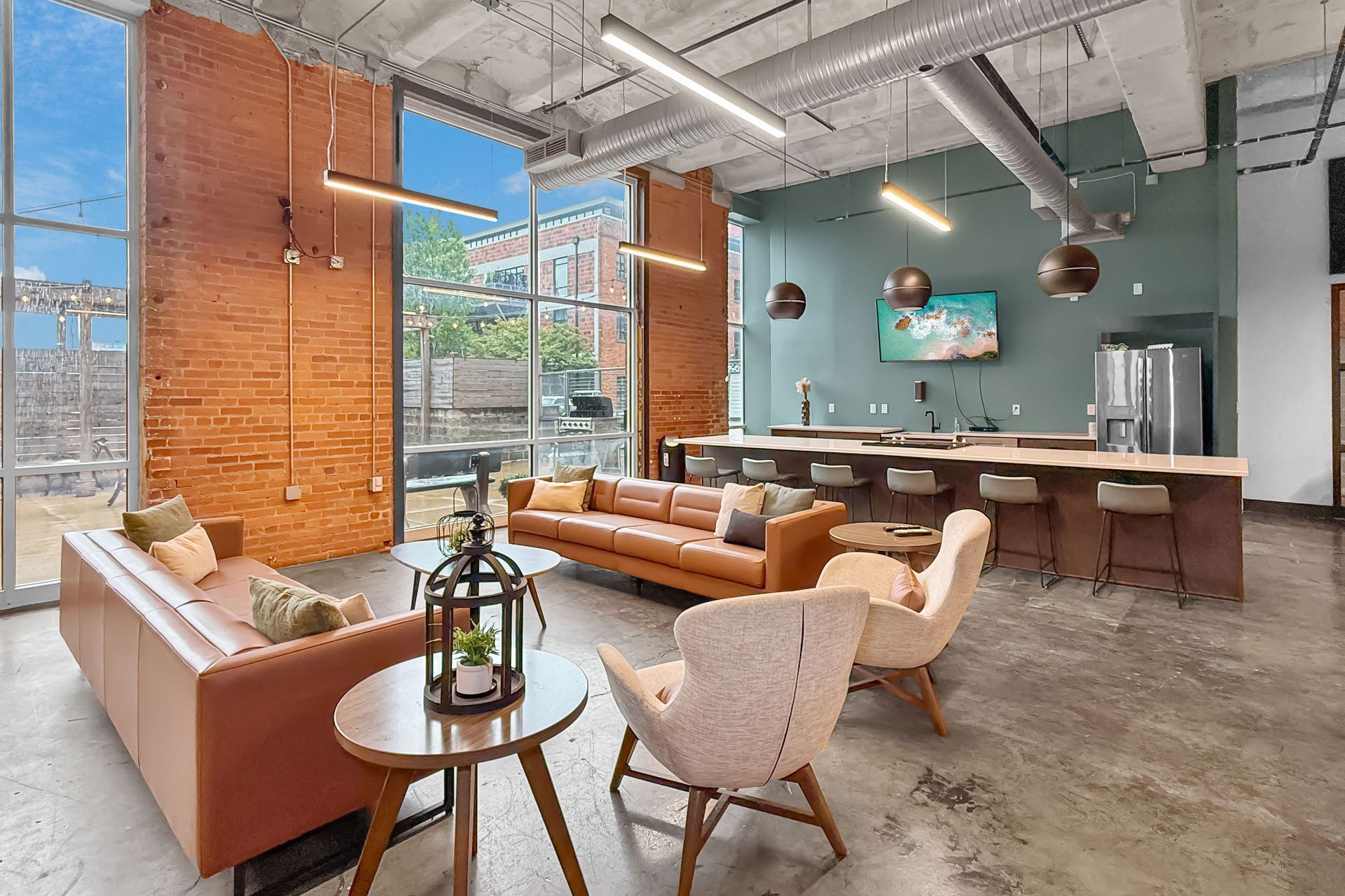 A bright, open-plan lounge with brown leather sofas, armchairs, and a bar area with stools against a teal wall.