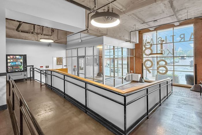 A modern interior space with a ramp leading to a glass-enclosed office, a vending machine, and large windows.