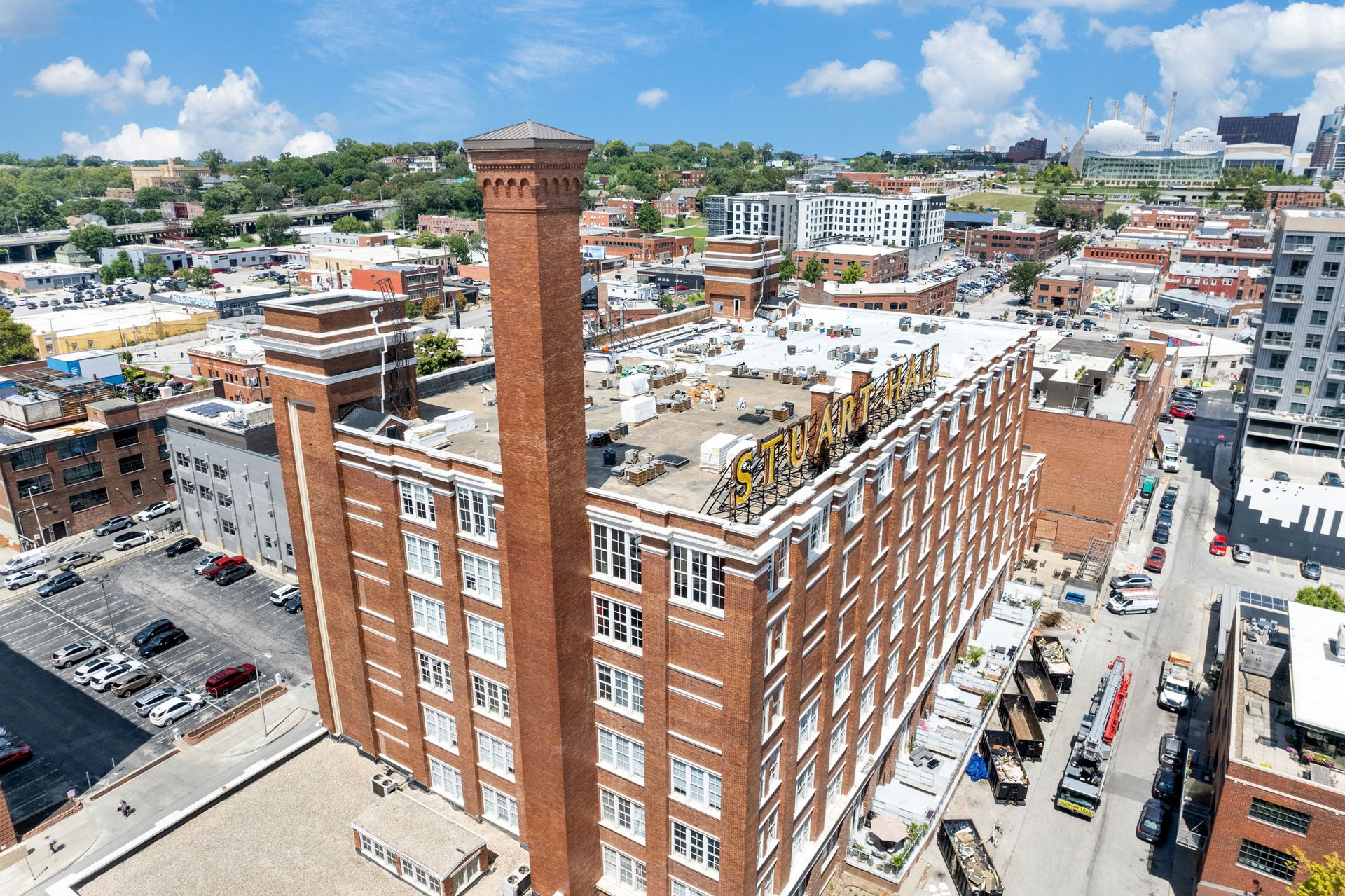 Aerial view of a tall, multi-story brick industrial building with a prominent smokestack in an urban setting.