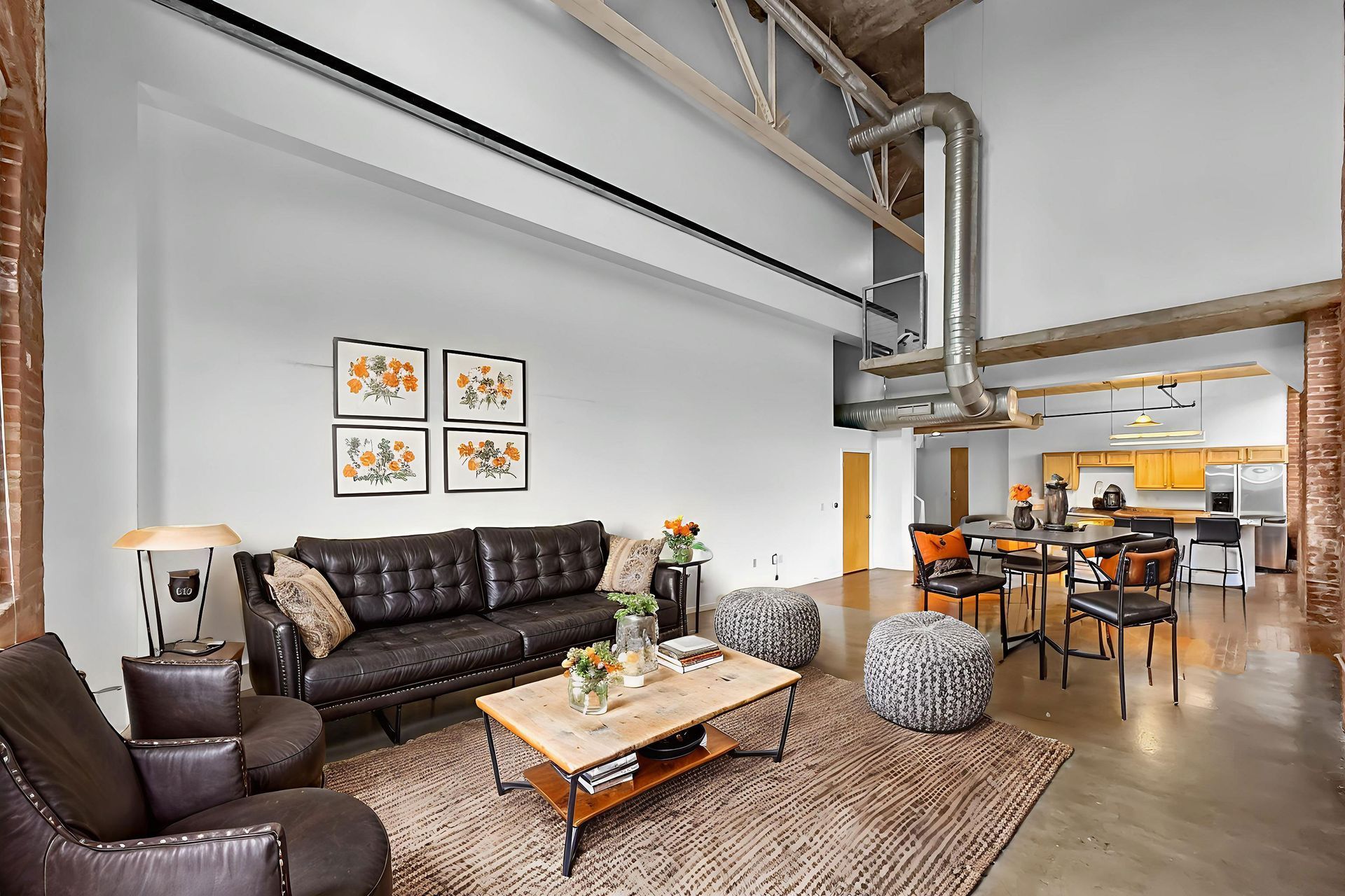 Modern loft apartment with an open floor plan, leather furniture, industrial metal ductwork, and concrete flooring.