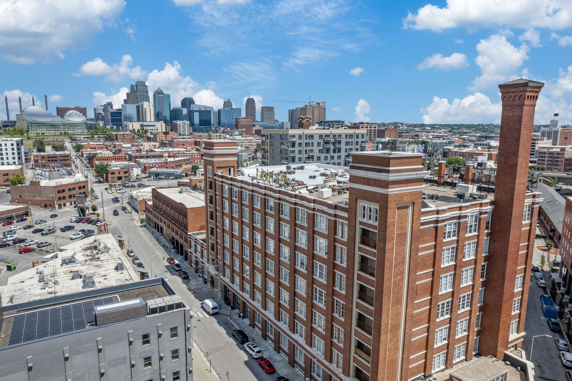 Aerial view of a tall, red-brick warehouse building with a prominent chimney, set against a modern city skyline.