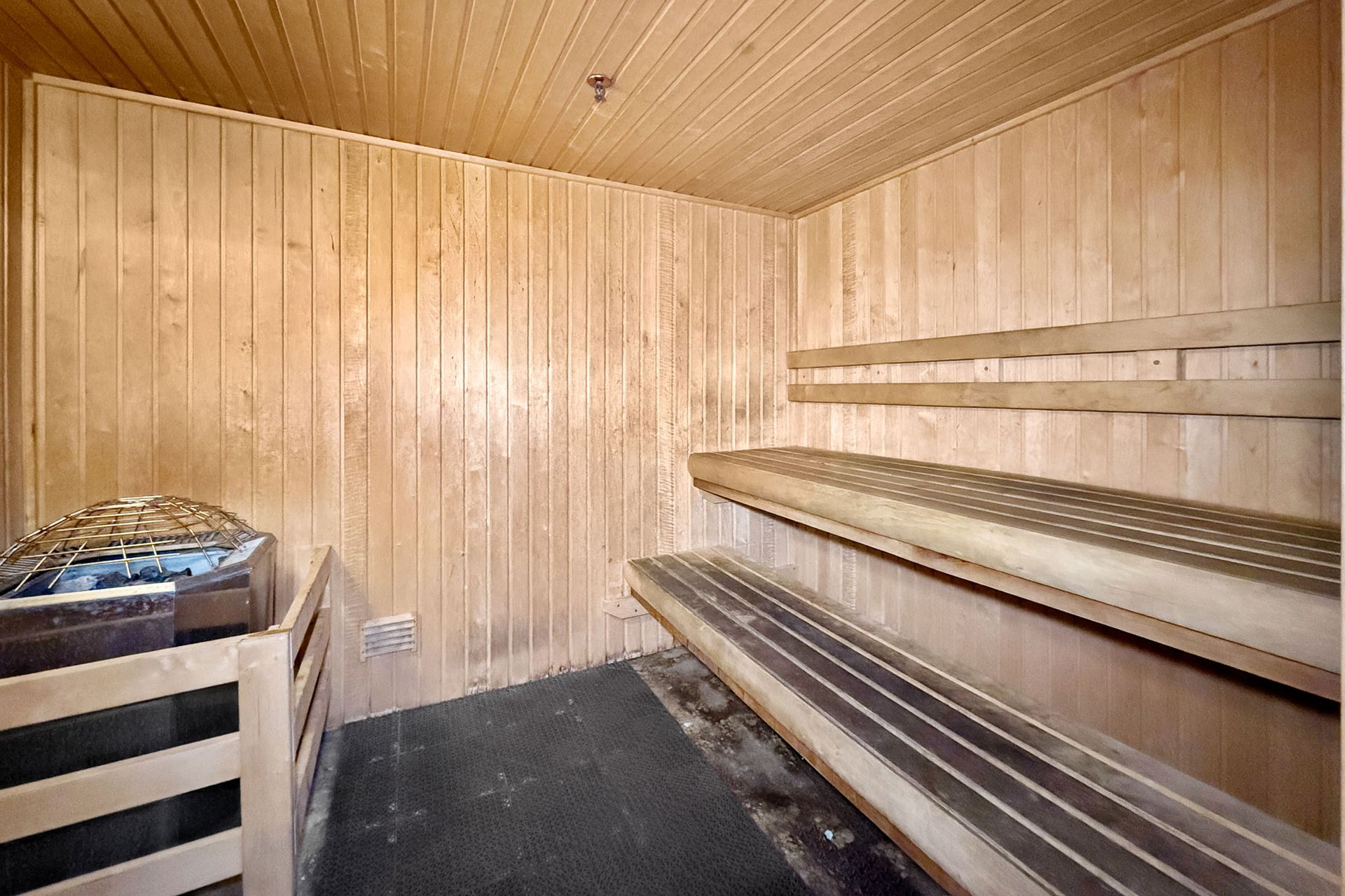 Interior view of a wooden sauna with tiered bench seating, wooden paneling, and a heater on the left.