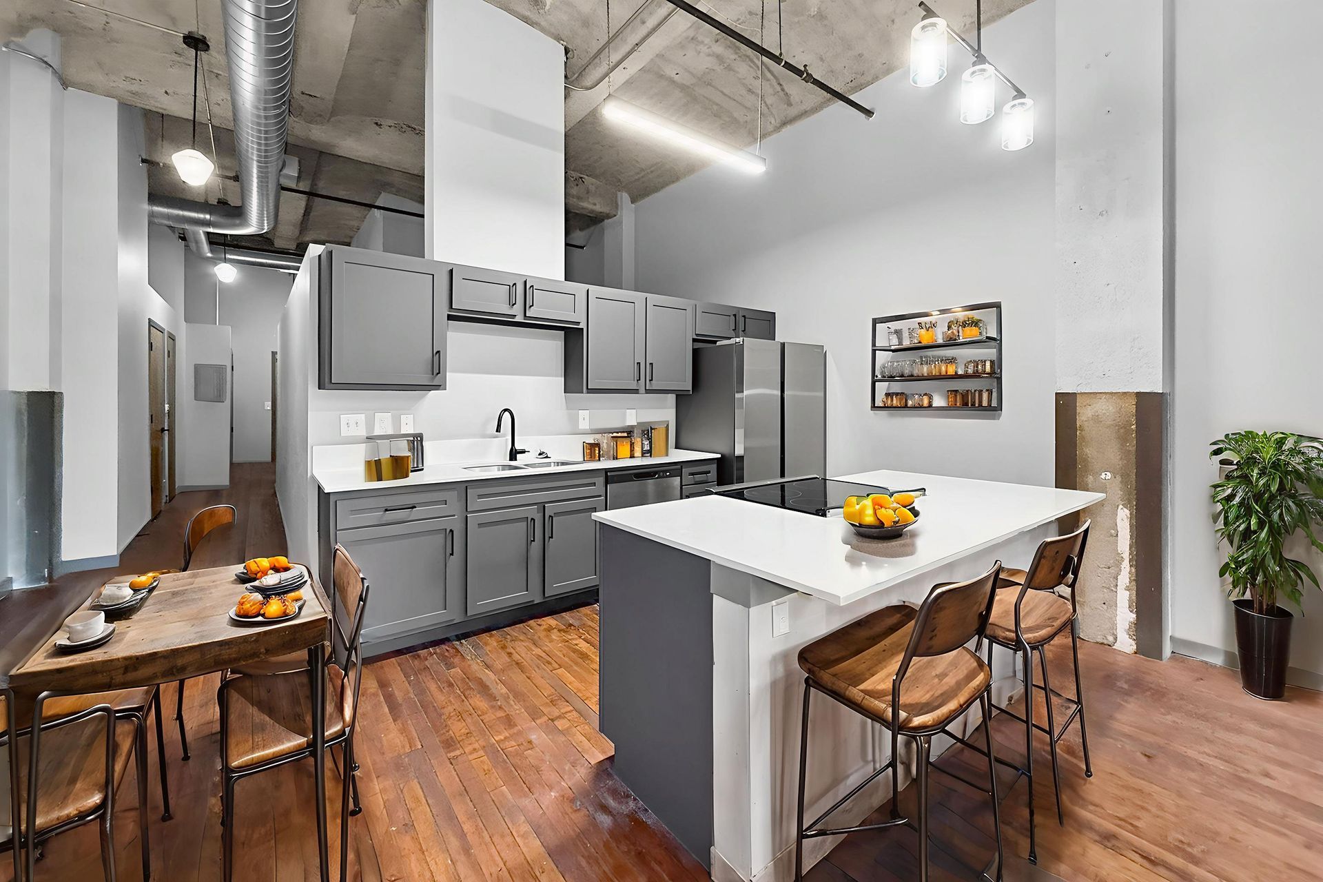 A modern kitchen with grey cabinetry, a white stone island with stools, a wooden dining table, and an open ceiling.