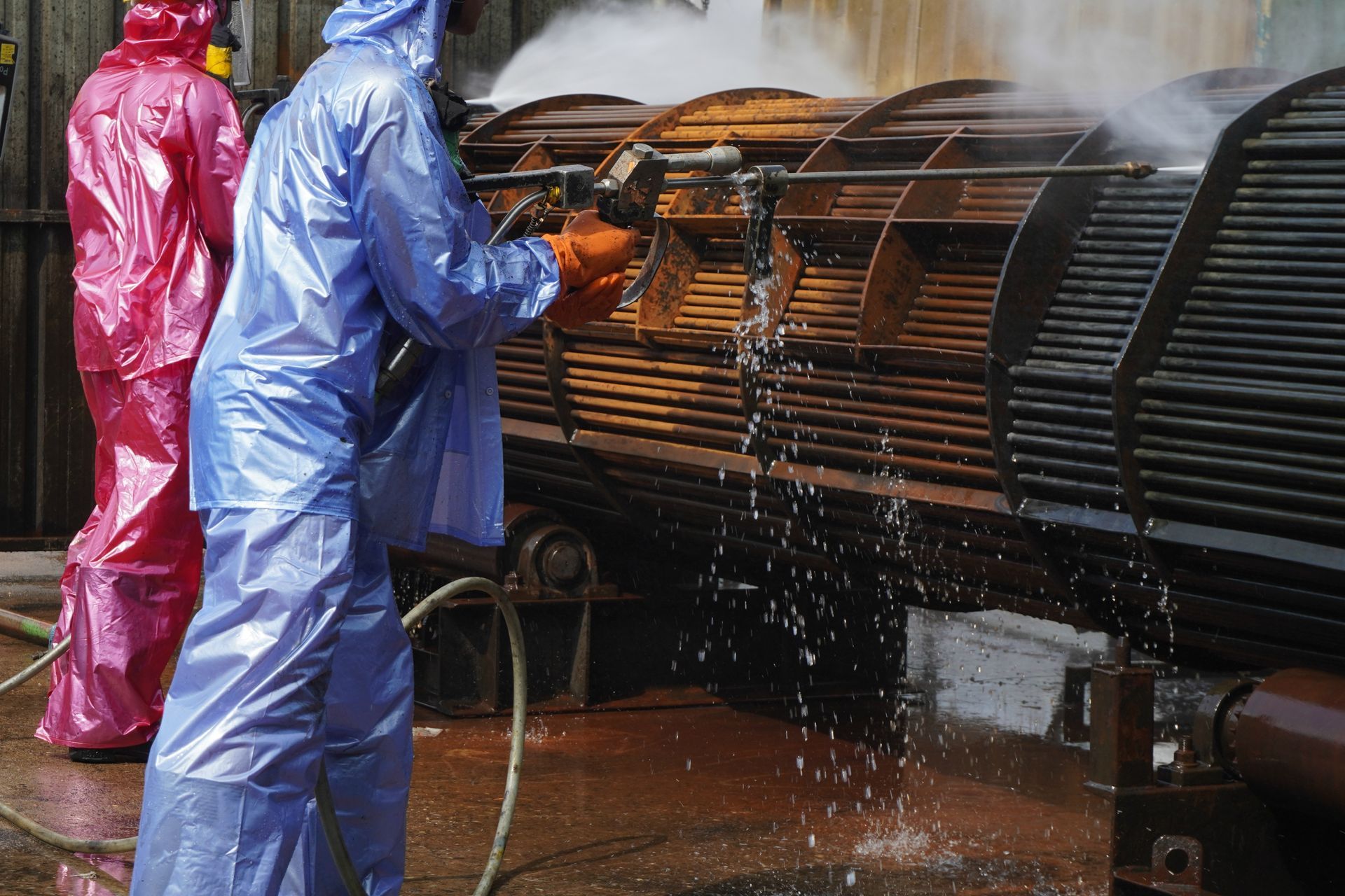 A man in a blue suit is cleaning a pipe with a hose.