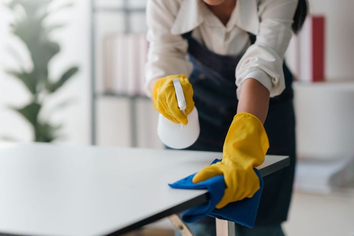 A woman wearing yellow gloves is cleaning a table with a cloth and spray bottle.