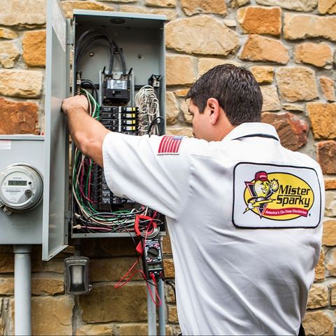 Mister Sparky Electrician in a white shirt fixes breaker panel