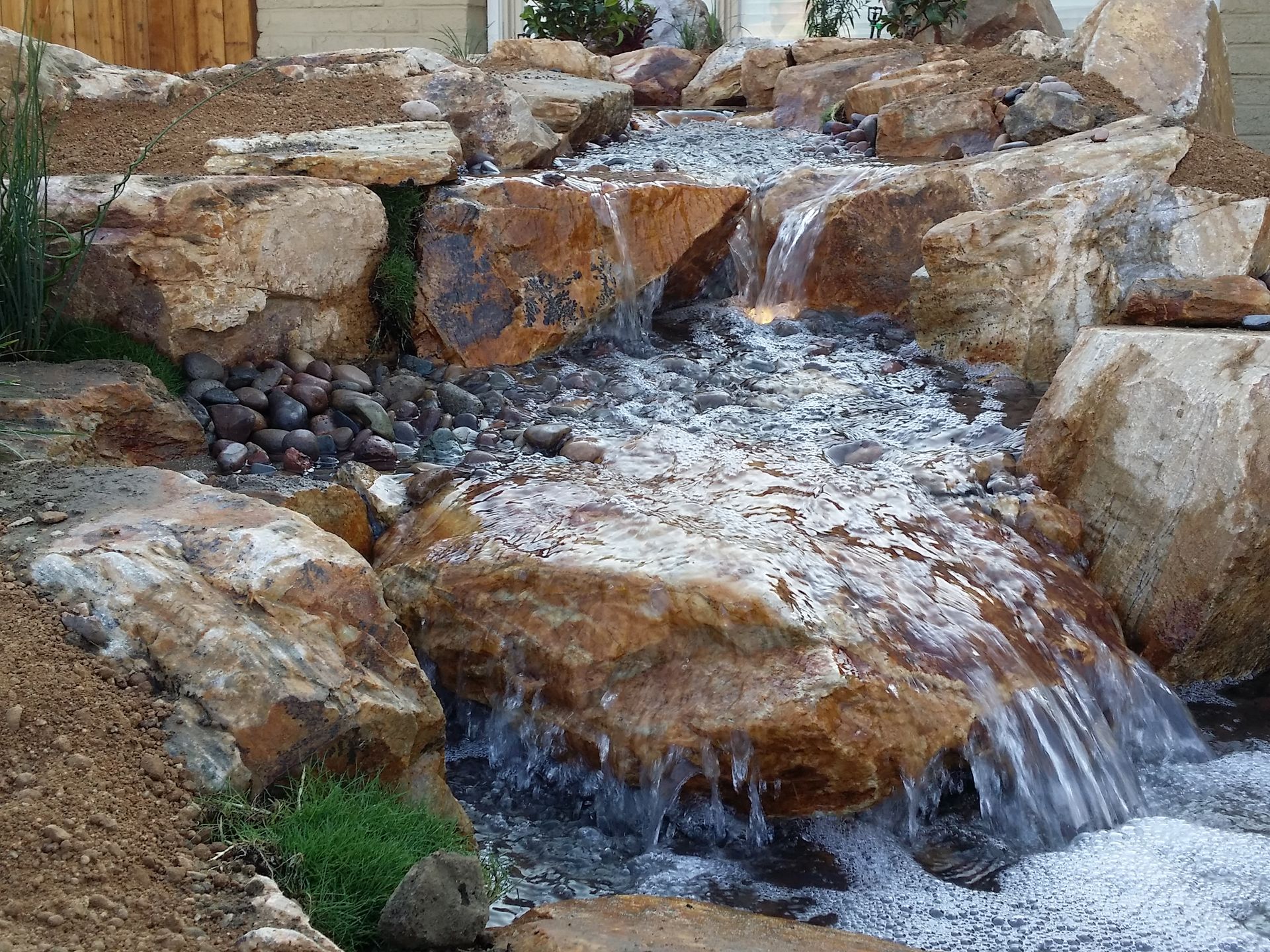 A small waterfall is surrounded by rocks and grass.