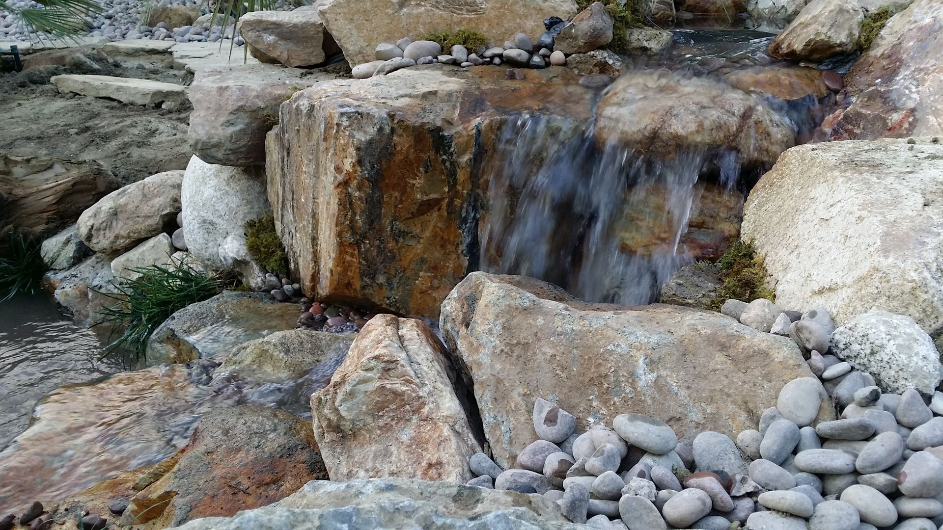 A small waterfall is surrounded by rocks and pebbles.