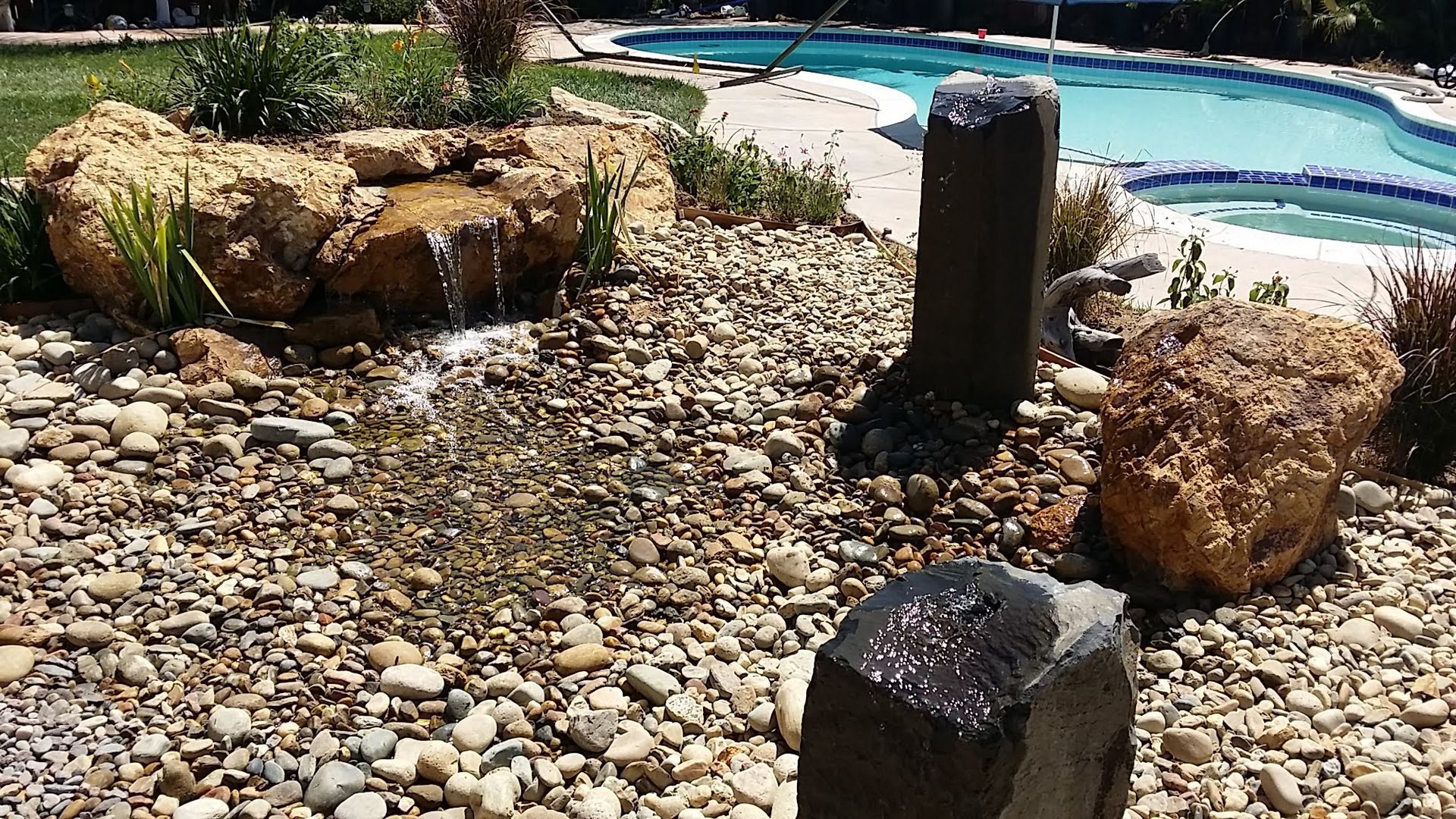 A swimming pool with a fountain and rocks in front of it.