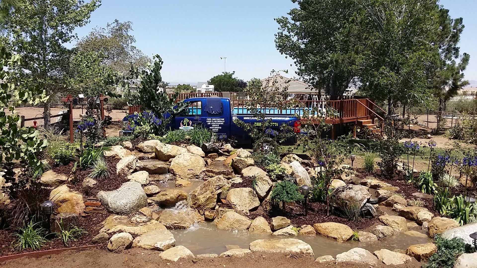 A blue truck is parked next to a waterfall in a garden.