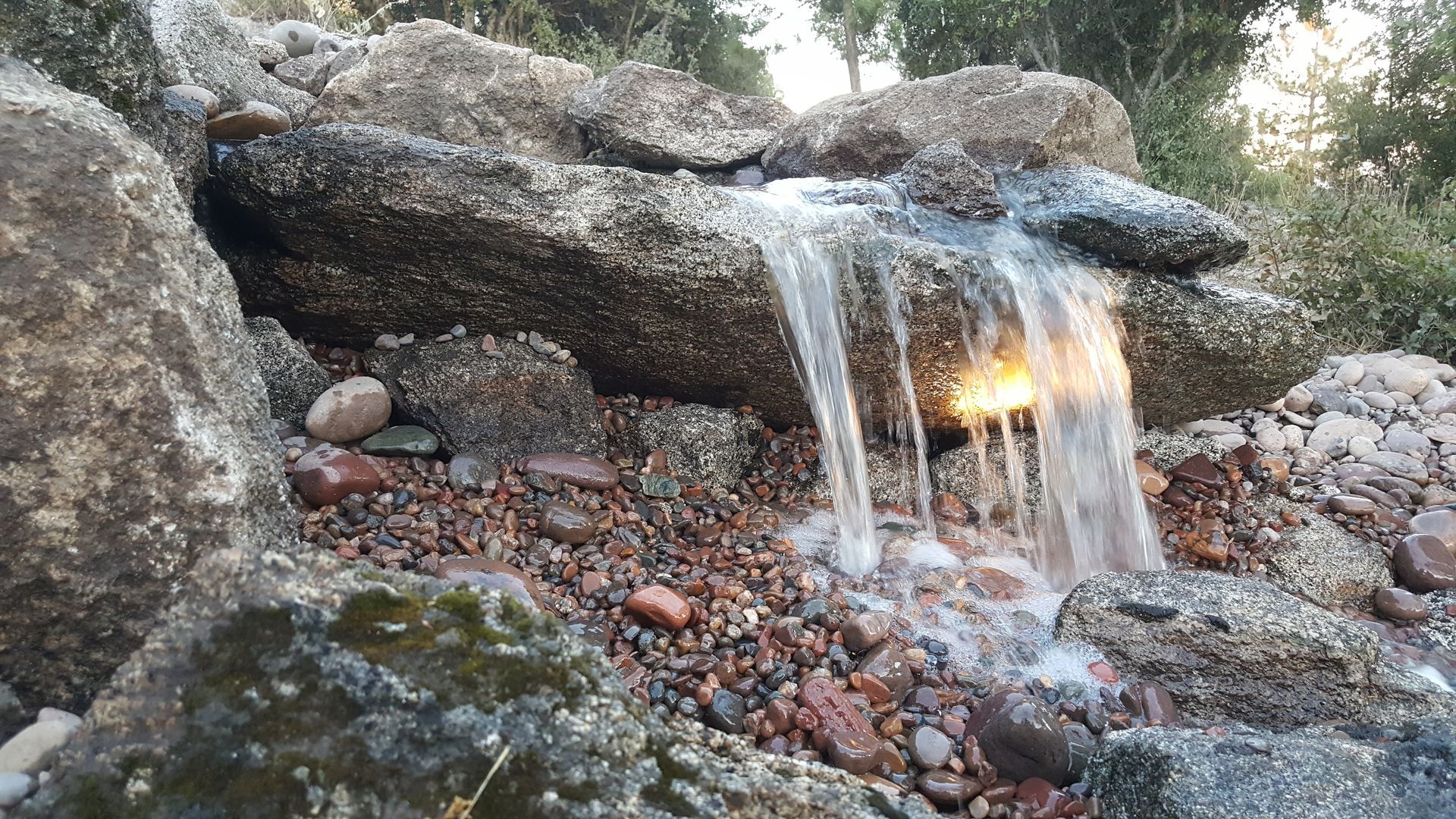 A small waterfall is surrounded by rocks and gravel.