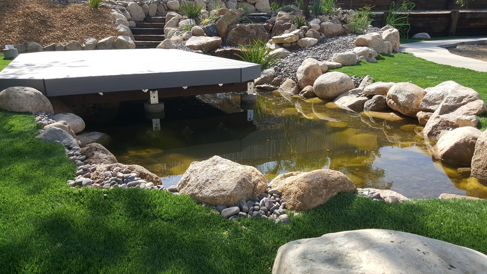 A pond surrounded by rocks and grass with a bridge over it