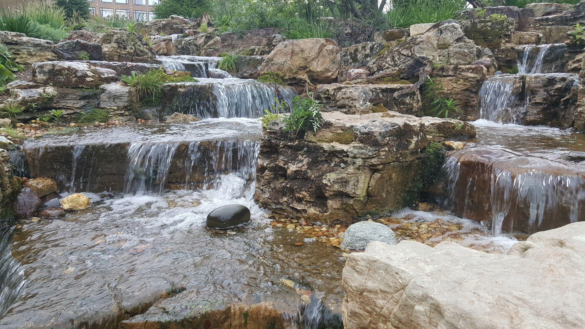 A waterfall is surrounded by rocks and trees in a park.