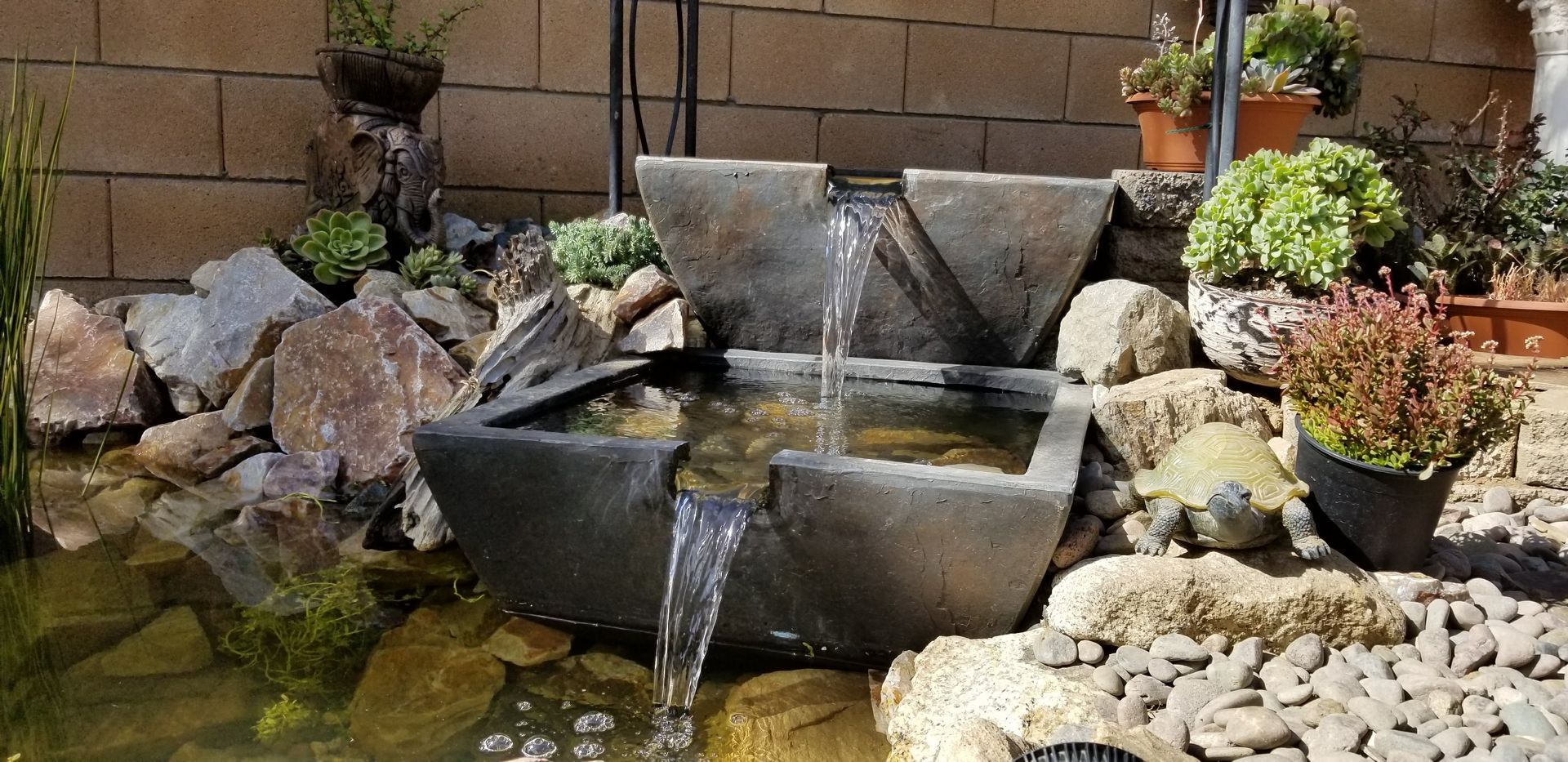 A pond with a waterfall in the middle of it surrounded by rocks and plants.