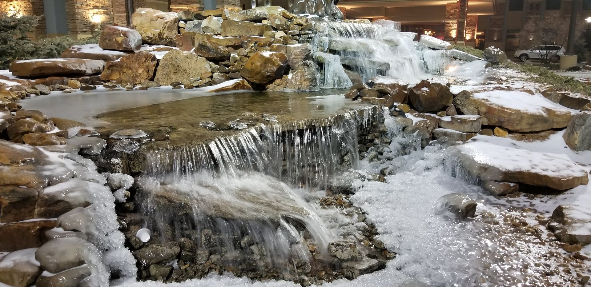 A waterfall is surrounded by rocks and ice and is covered in snow.