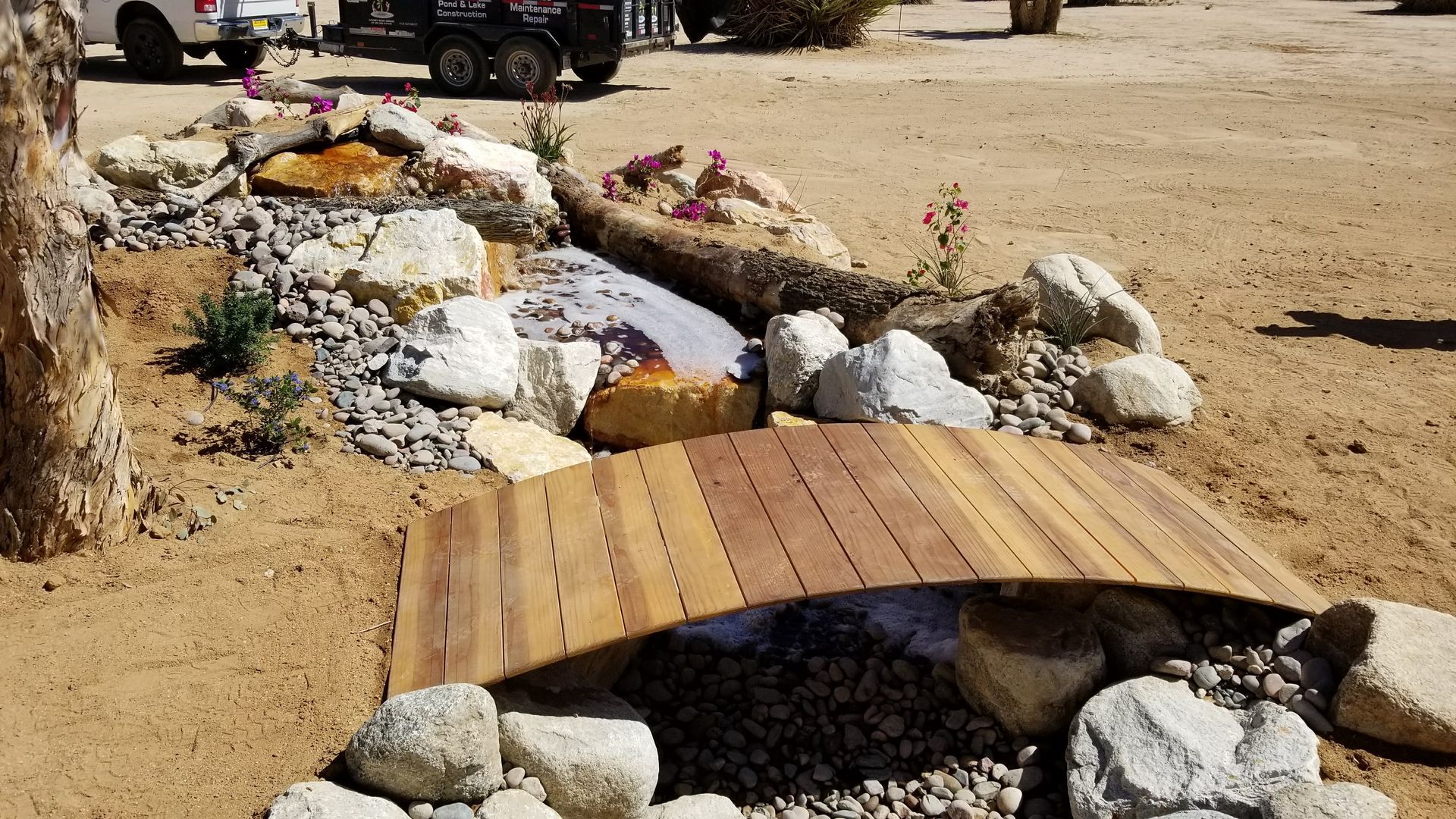 A wooden bridge over a stream surrounded by rocks and dirt.