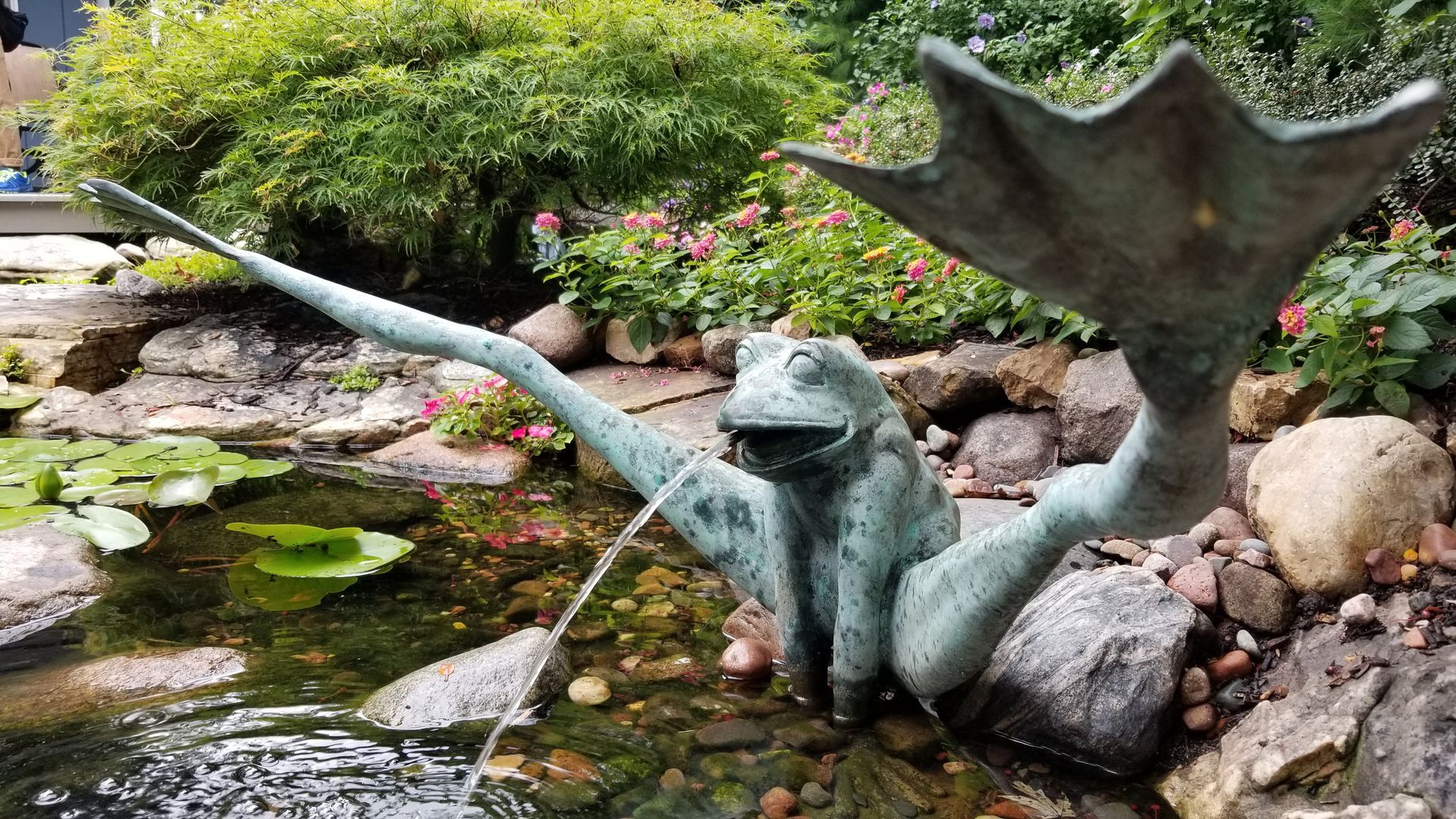 A frog statue is sitting on a rock next to a pond.