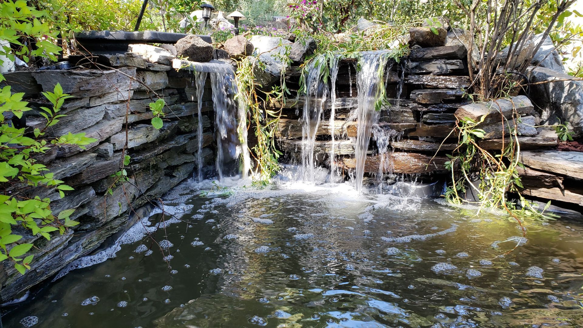 There is a waterfall in the middle of a pond surrounded by rocks.