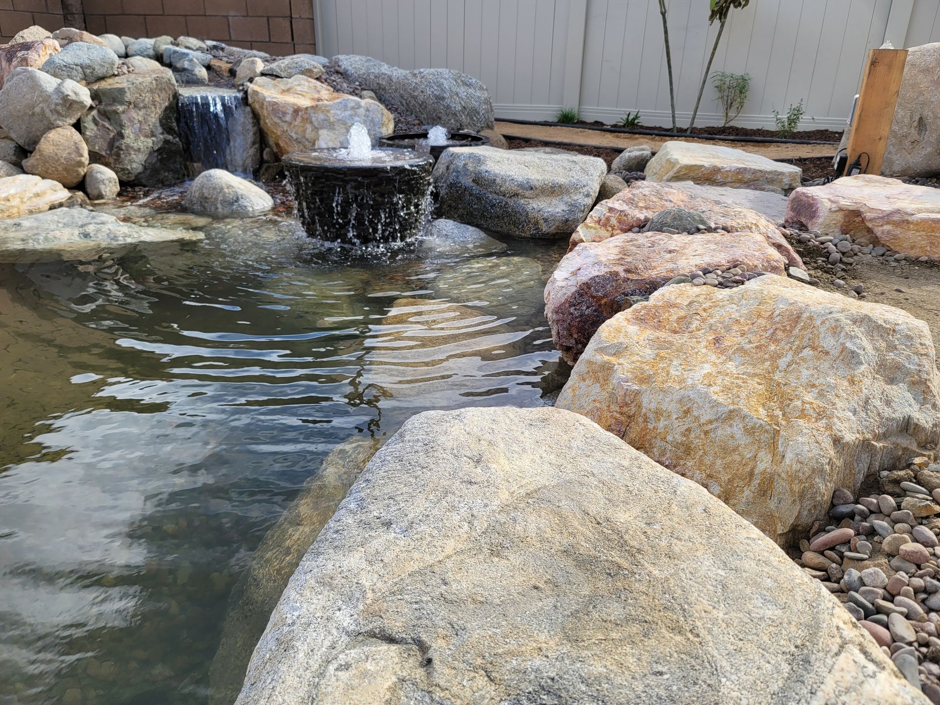 There is a waterfall in the middle of the pond surrounded by rocks.