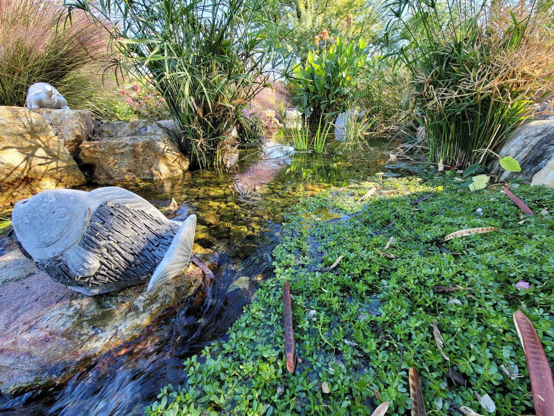 A statue of an elephant is sitting on a rock next to a pond.
