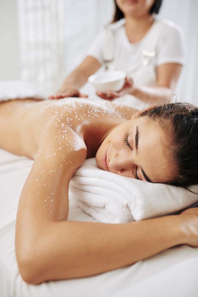 Worker Applying Salt Scrub on Back of Young Woman — Traditional Massage Services In Broadbeach, QLD