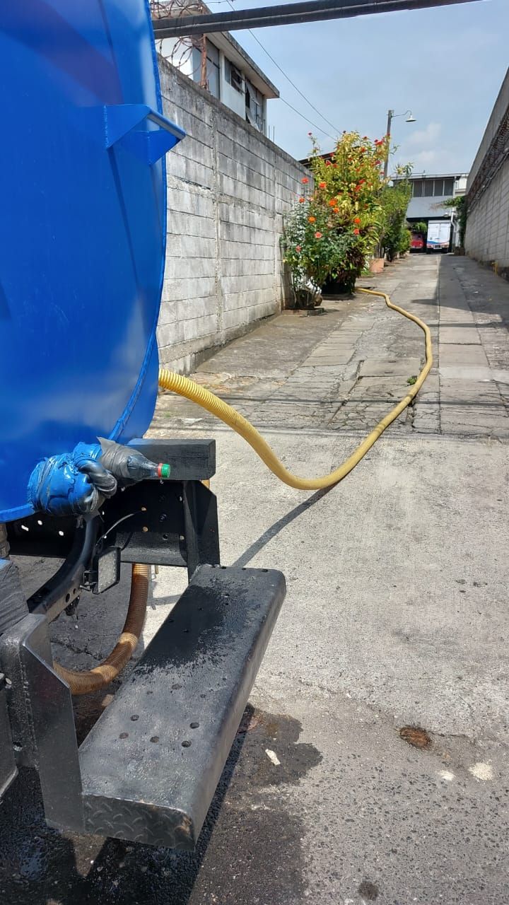 Camión de agua azul con una manguera amarilla que se extiende por un callejón estrecho.