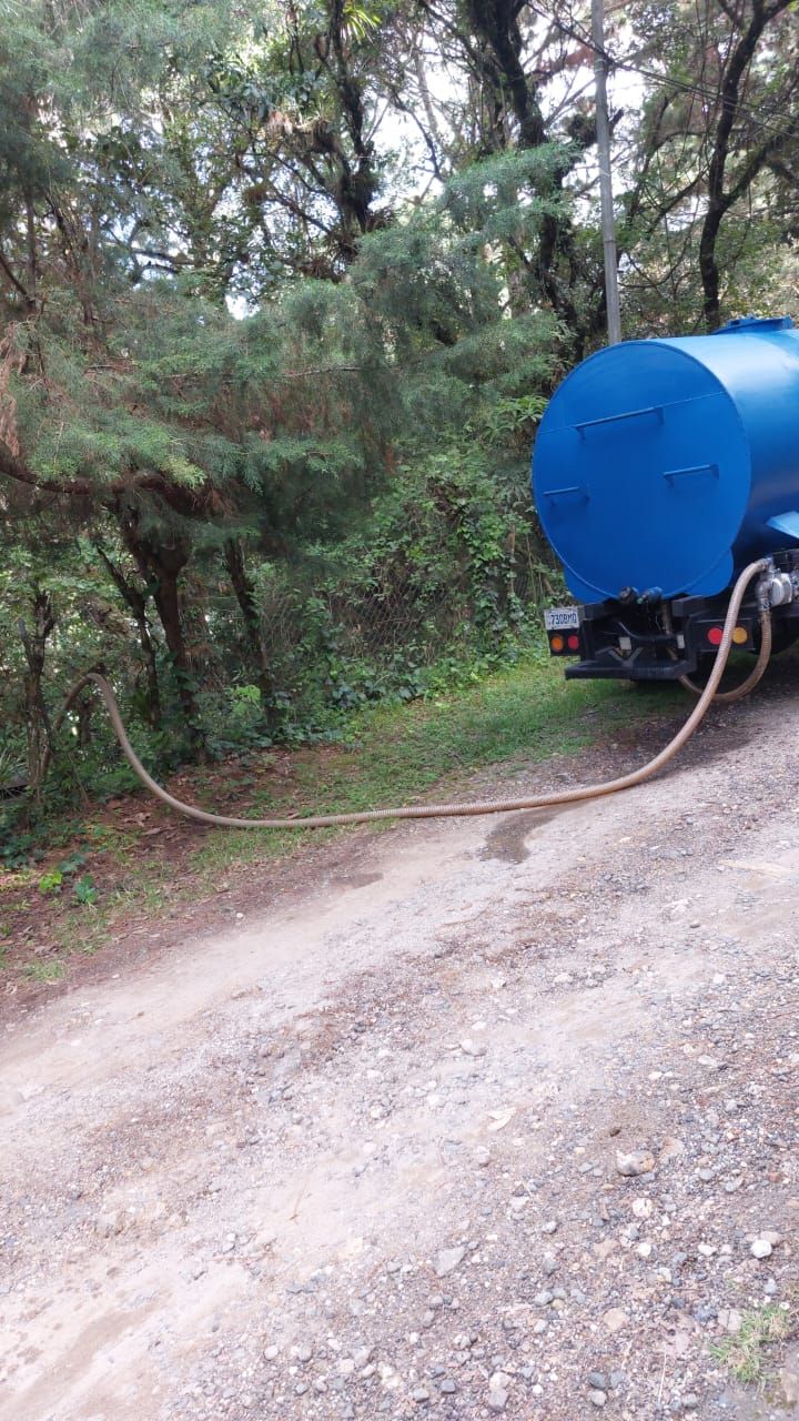 Camión de agua azul en camino de tierra con manguera extendida hacia los árboles.