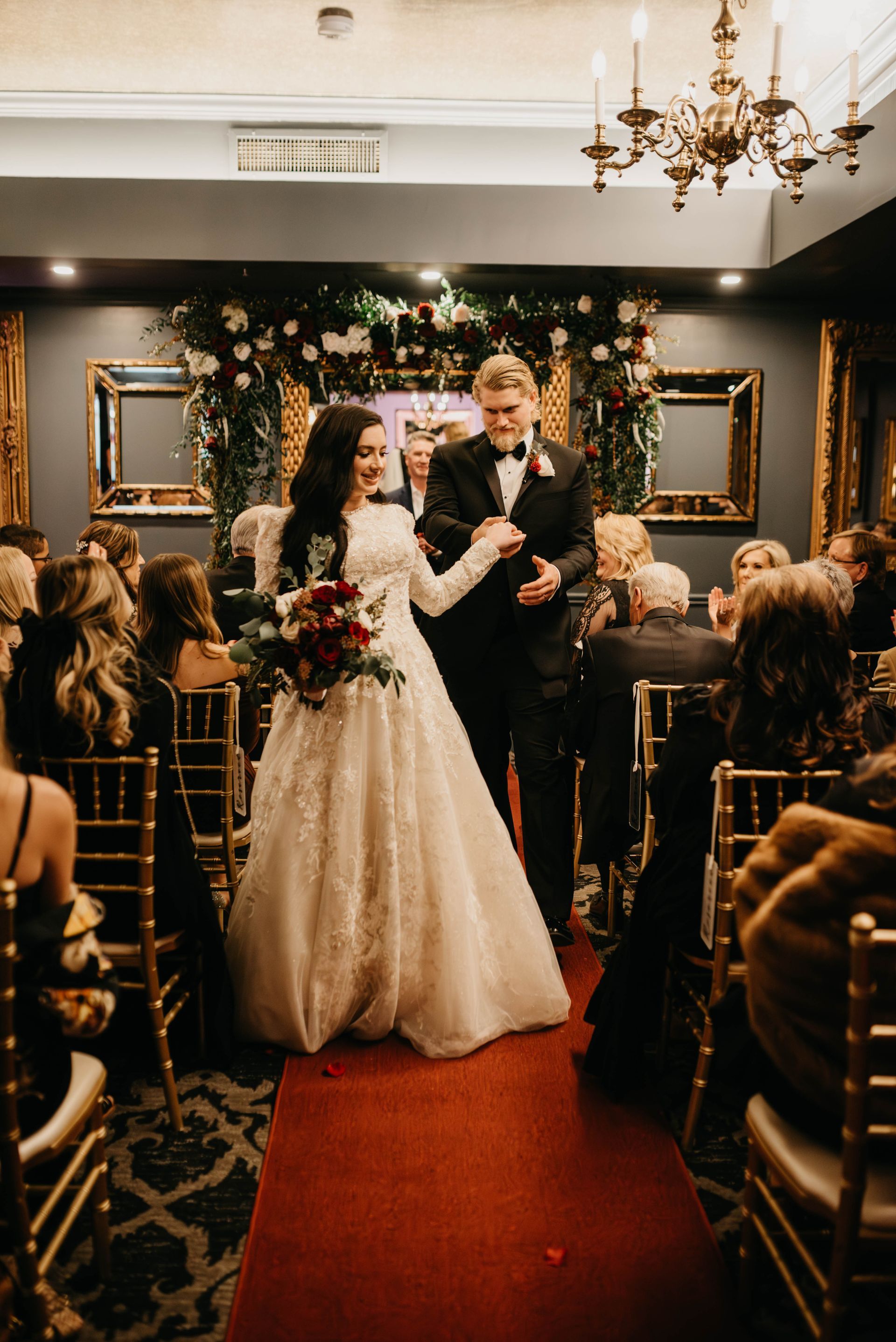 Bride and groom walking down red carpet aisle, decorated wedding ceremony.