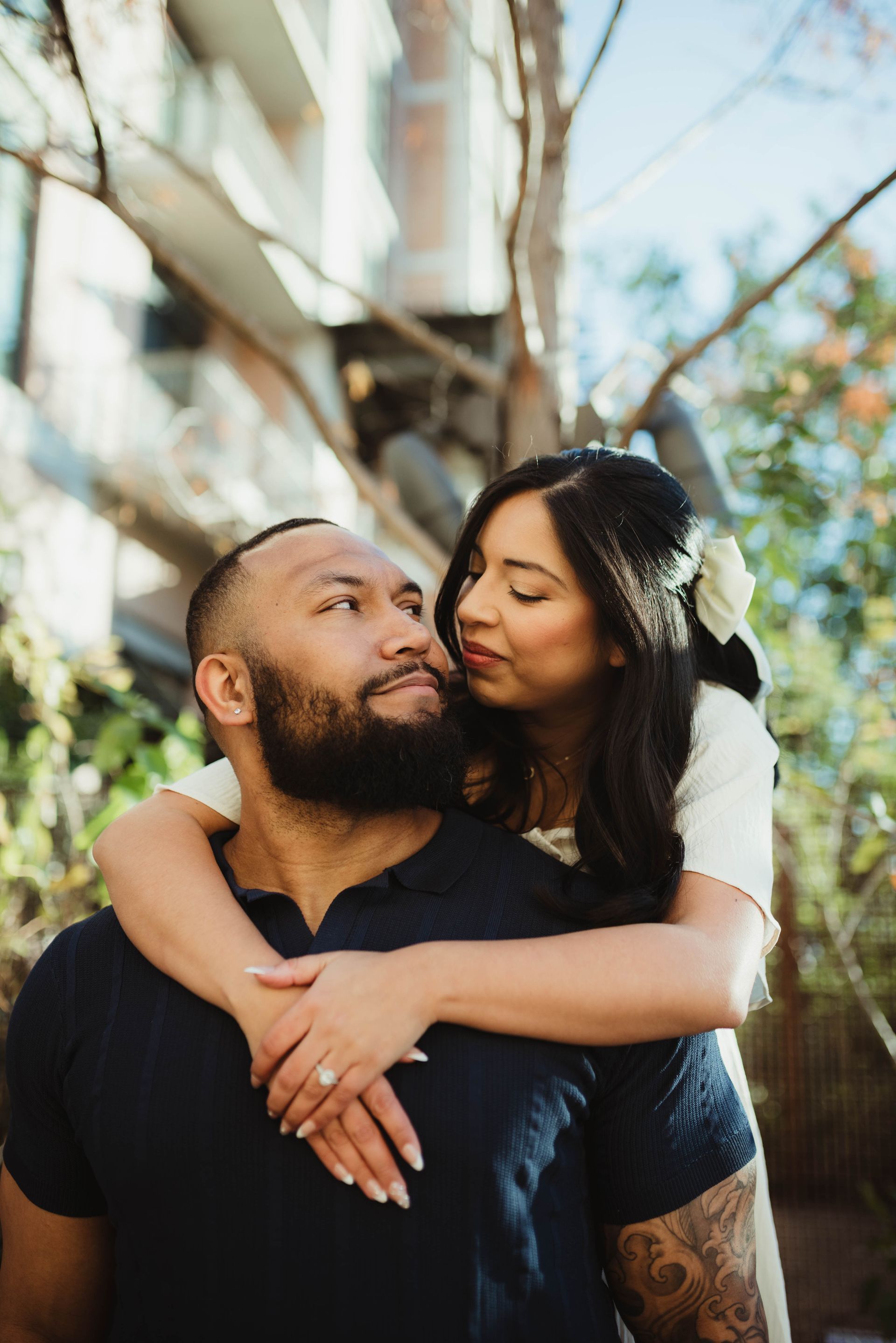 Couple embracing outdoors; woman with flower in hair, man with beard, looking at each other.