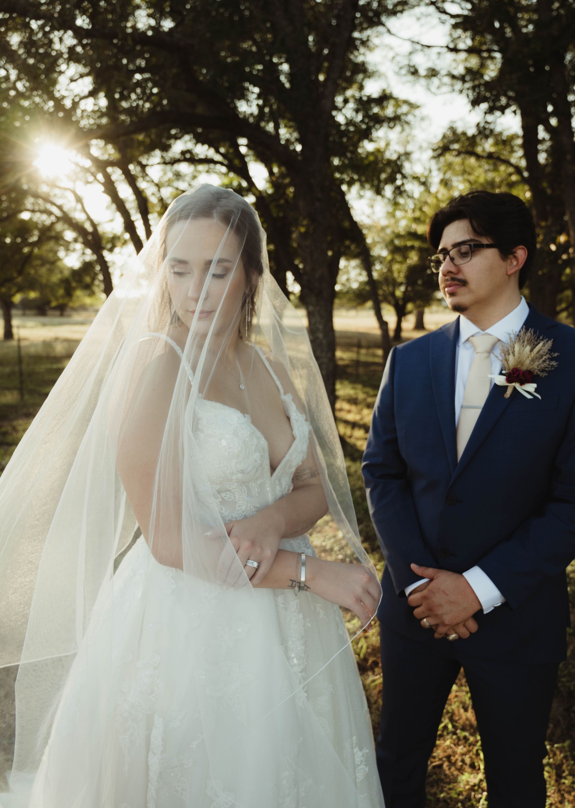 Bride in white dress, veil, and groom in blue suit standing outdoors.