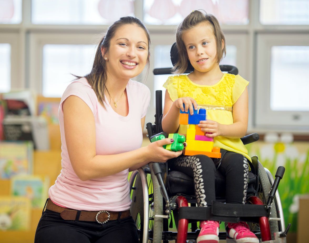 Woman smiling with child that has cerebral palsy playing with building block toys