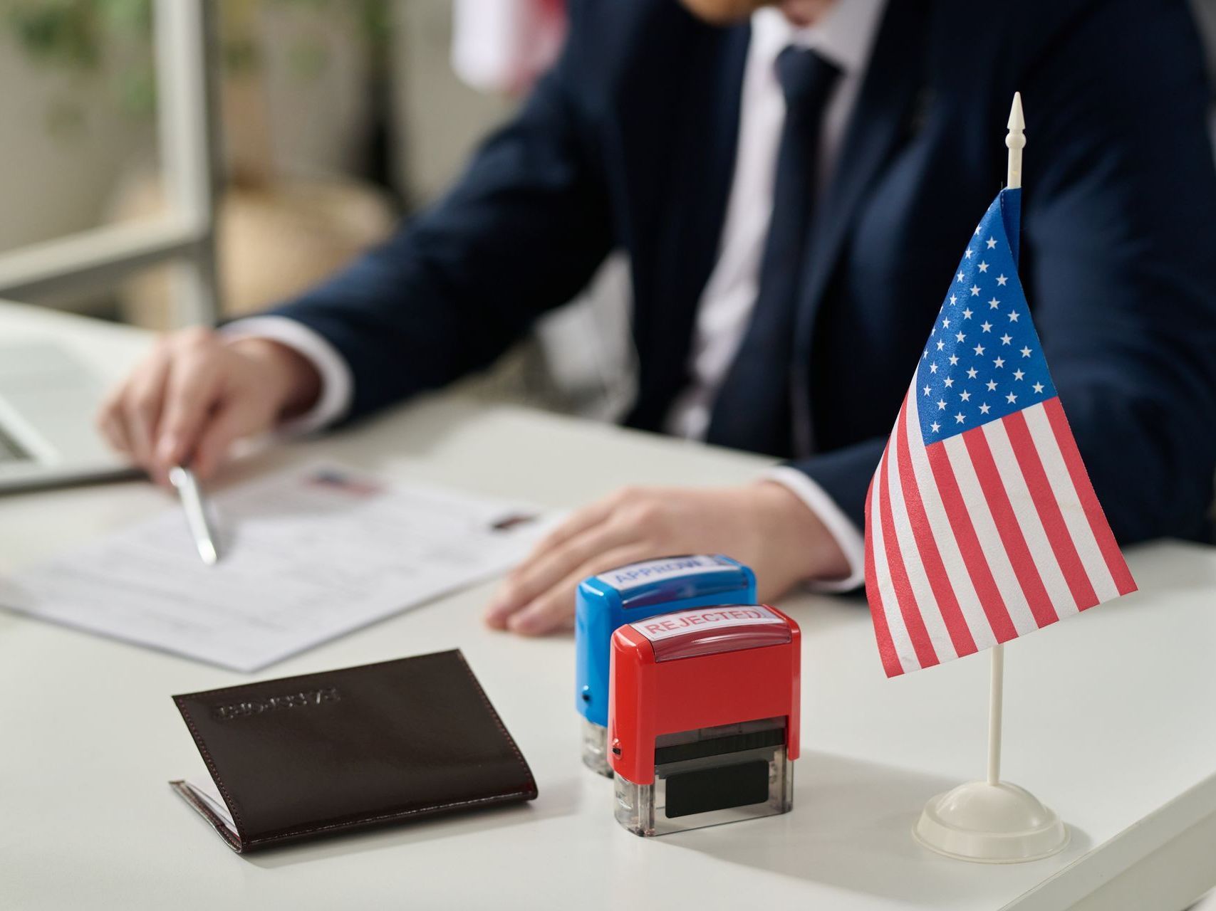 A man in a suit is sitting at a desk with a small american flag.