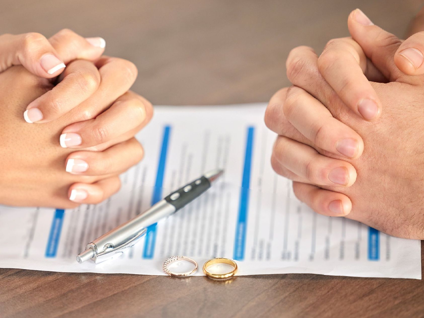 A man and a woman are sitting at a table with their hands folded.