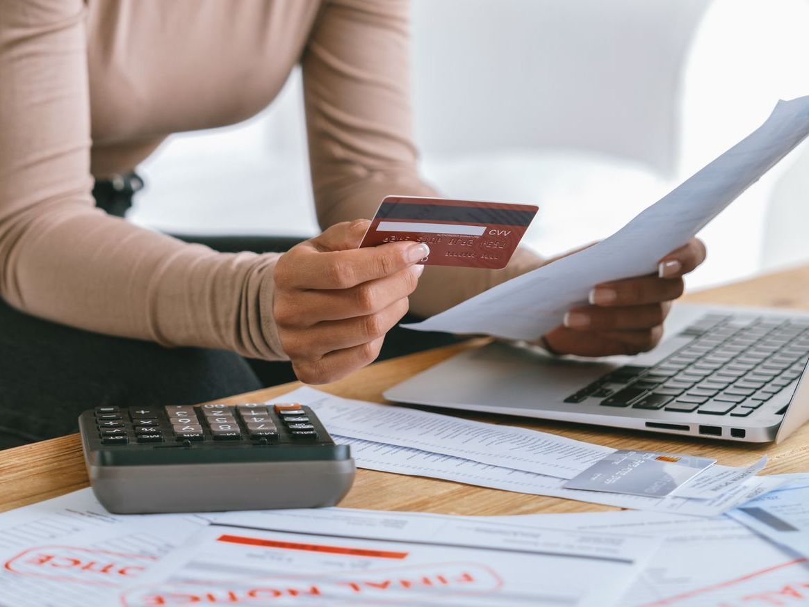 A woman is holding a credit card and a piece of paper in front of a laptop.