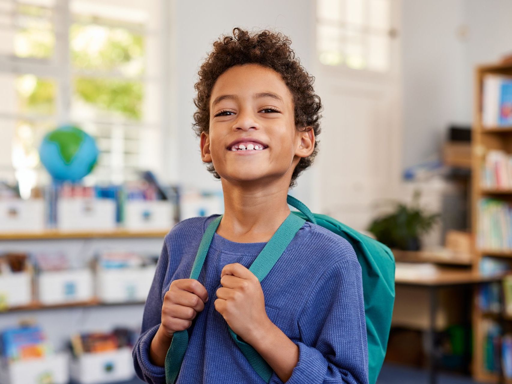 A young boy with a backpack is smiling in a classroom.