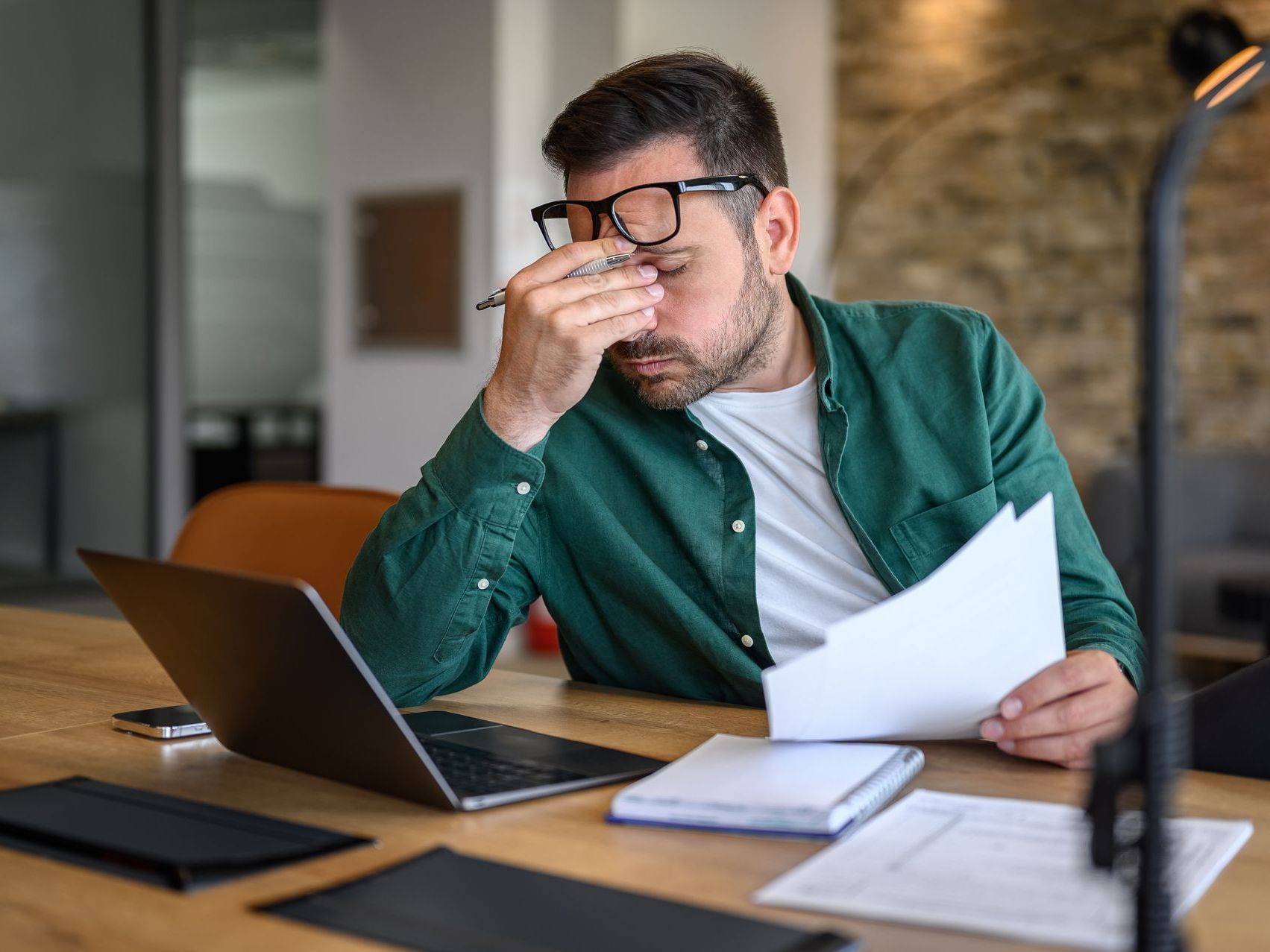 A man is sitting at a desk with a laptop and a piece of paper.