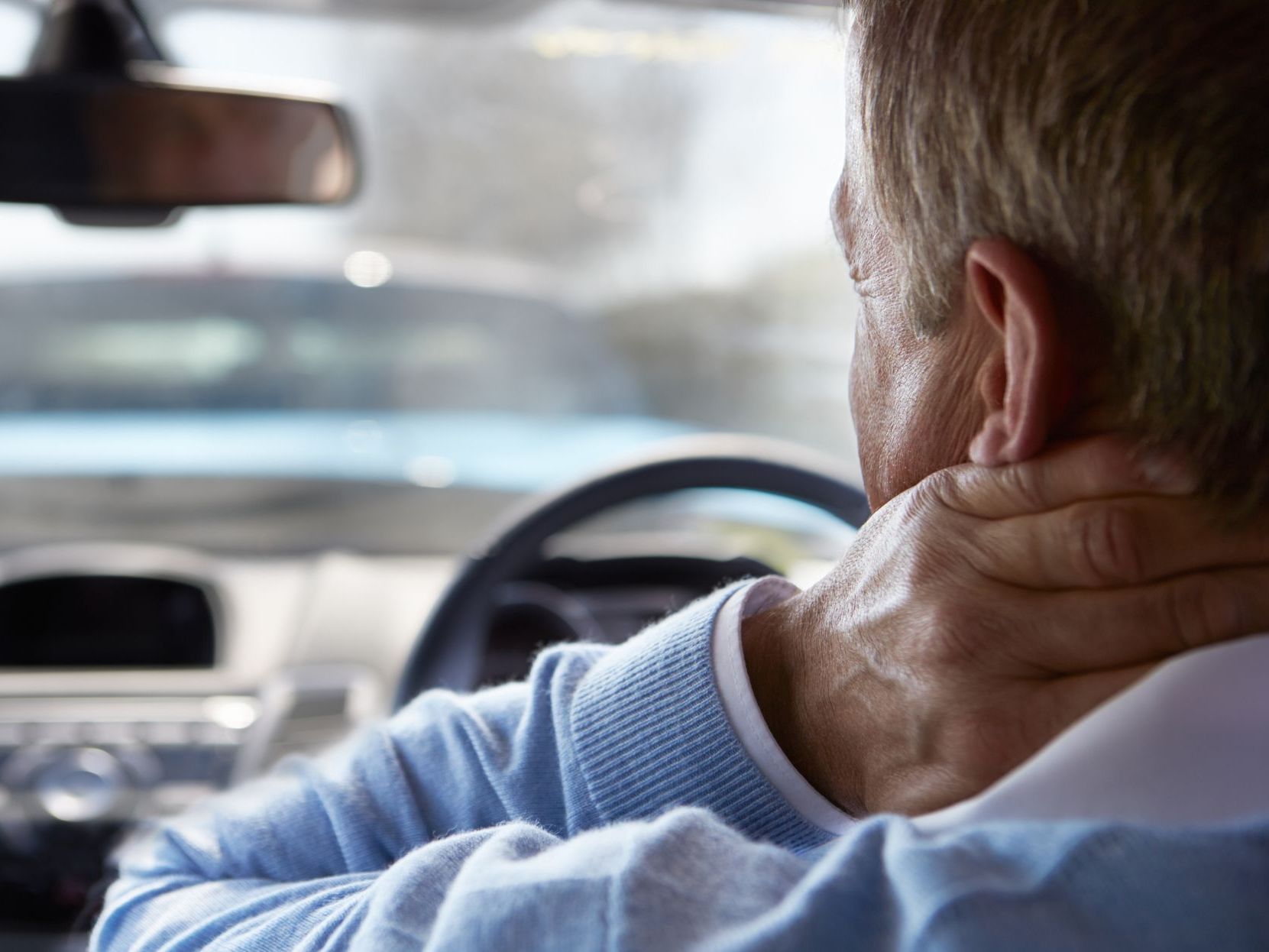 A man is holding his neck in pain while driving a car.