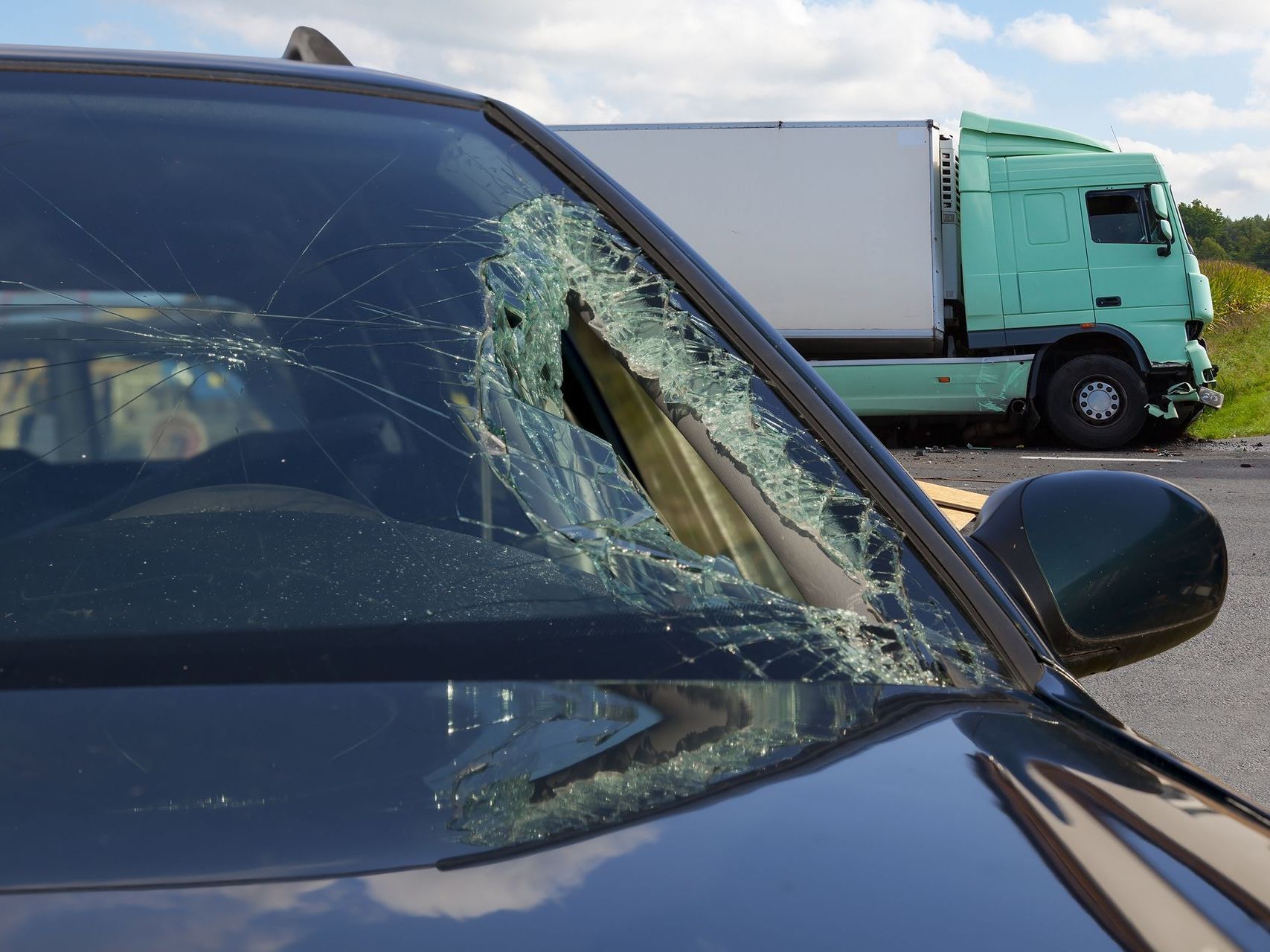 A car with a broken windshield and a truck in the background