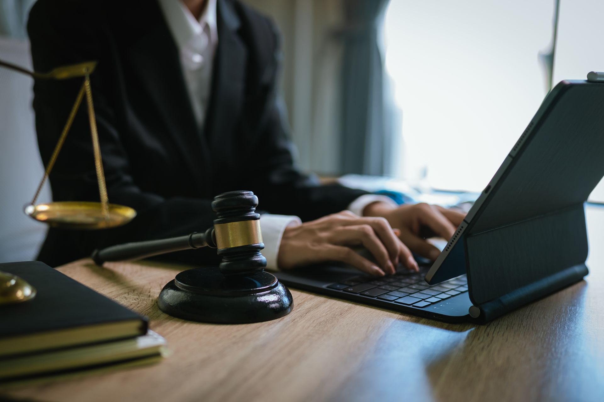 Attorney working on a laptop at a desk with a gavel and legal scales nearby.