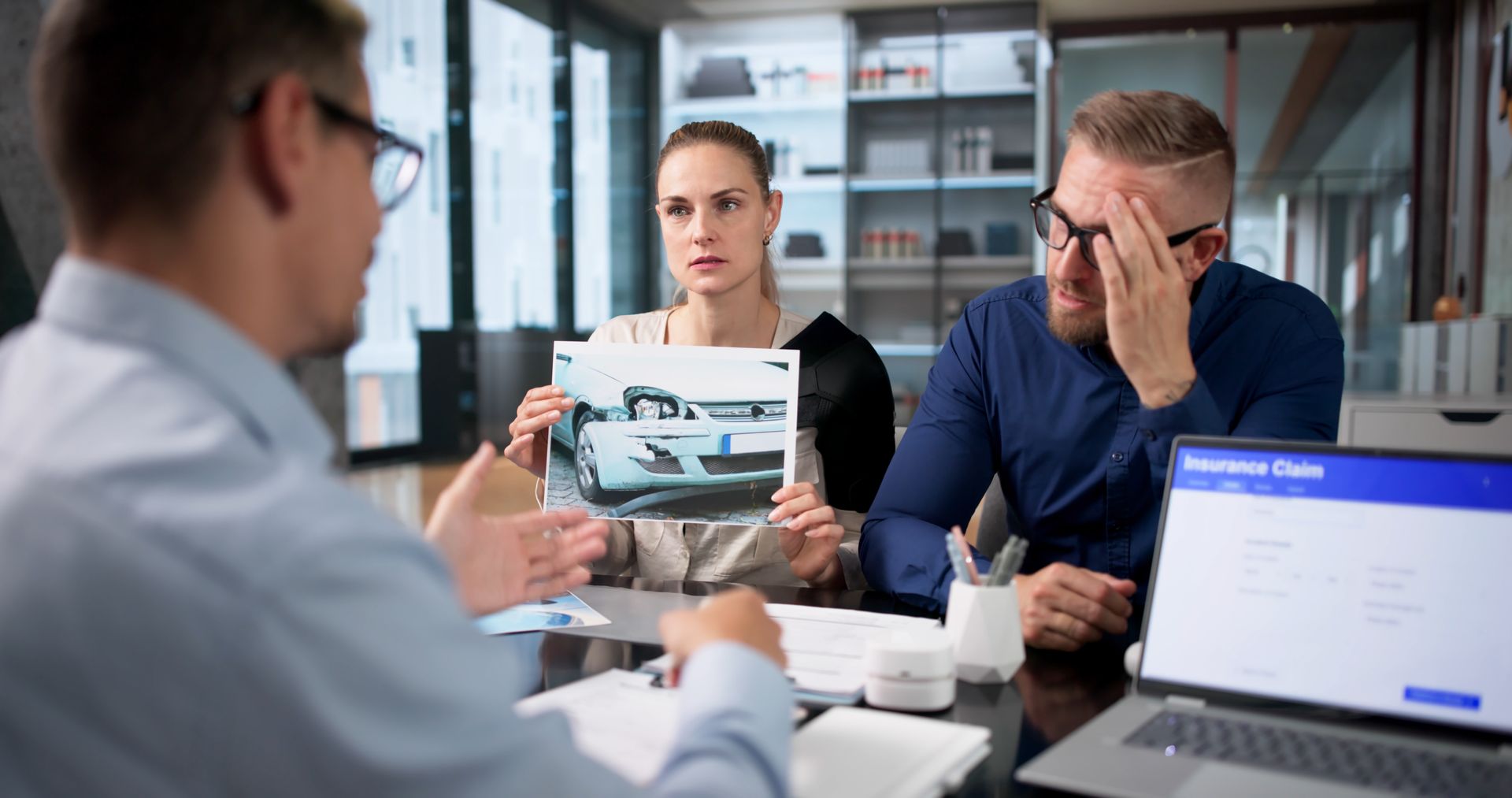 Business meeting in an office, with a tablet showing a car and a laptop open beside three people discussing. Business meeting in an office, with a tablet showing a car and a laptop open beside three people discussing.
