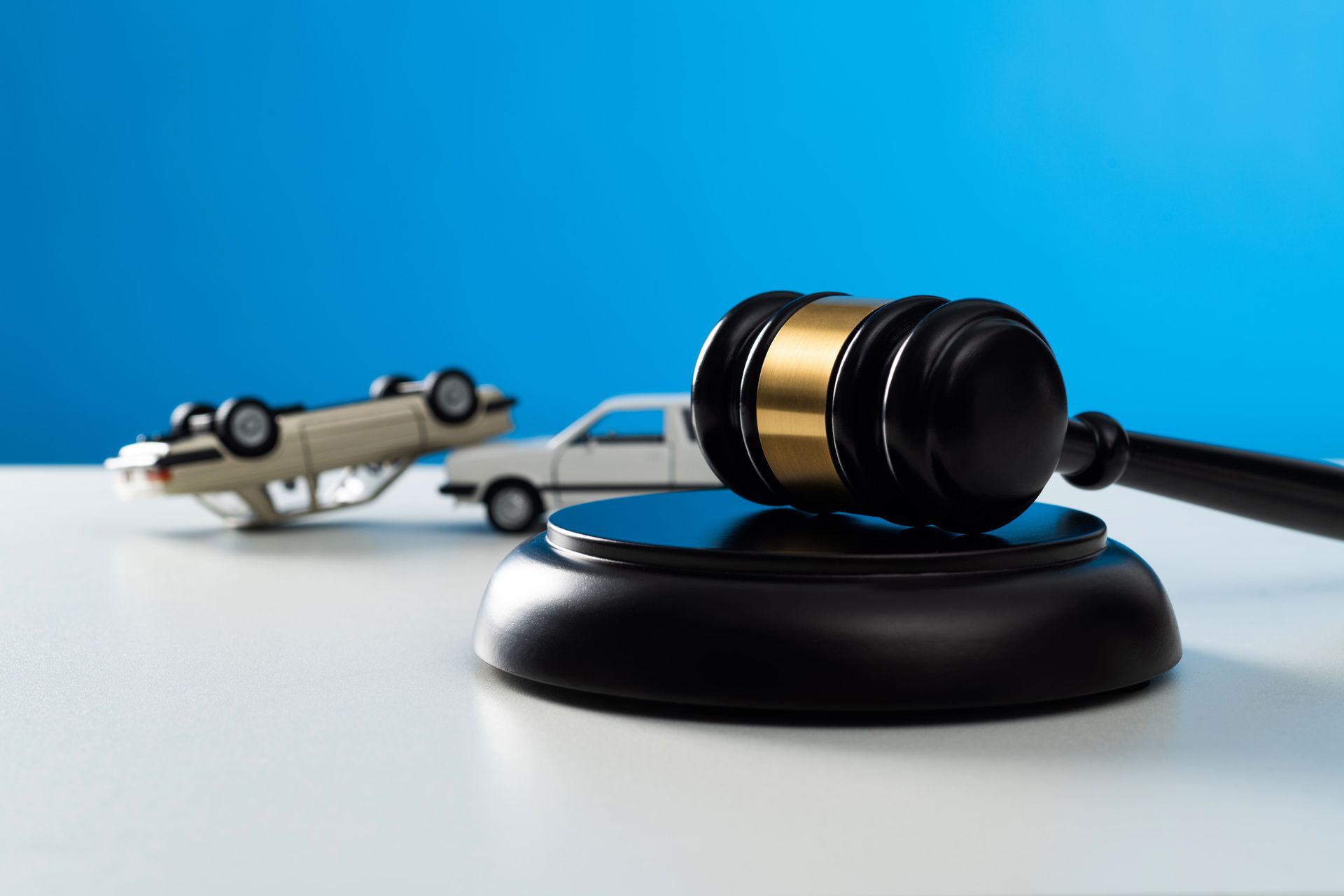 A wooden gavel and two white model cars in the background on a table.